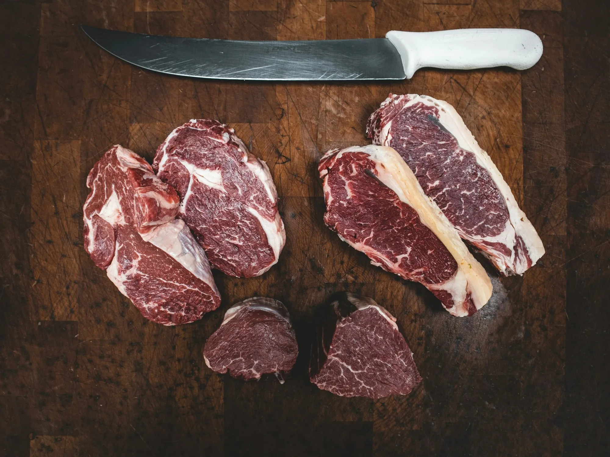 Ribeye and strip steaks with a butcher knife on a wood block (stock photo)