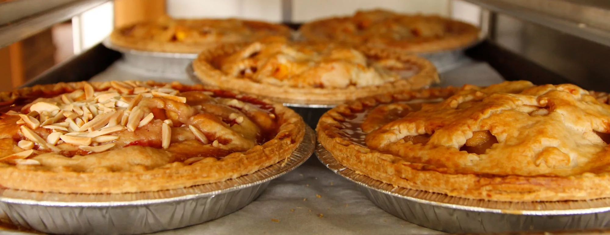 Fresh-baked fruit pies, one topped with sliced almonds, cooling on racks