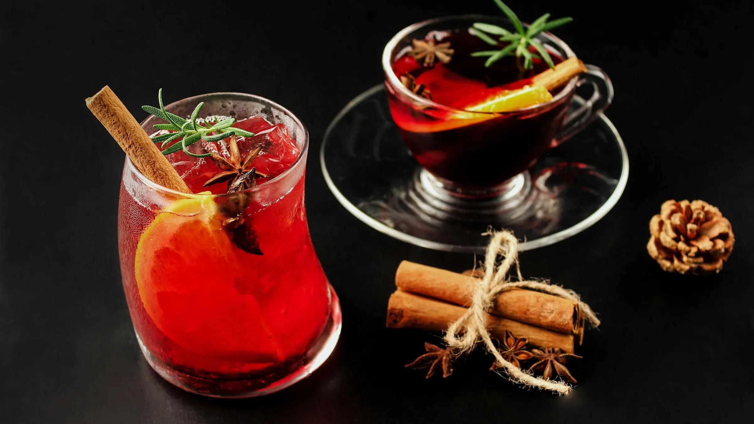 A red autumn drink with orange, cinnamon and rosemary on a dark table