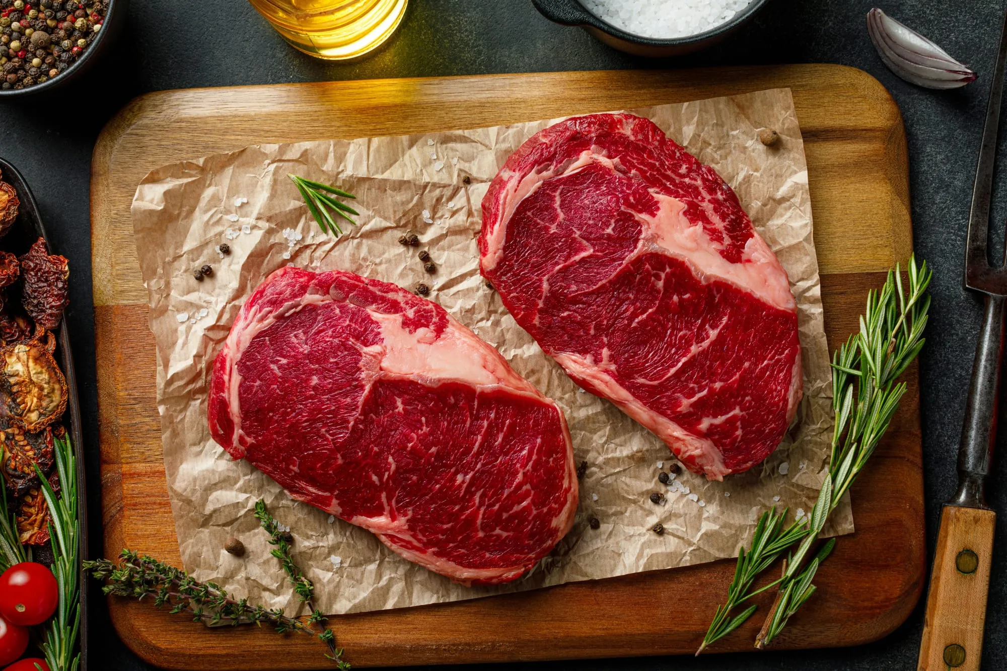 Two raw marbled steaks on butcher paper with rosemary and peppercorns (stock photo)