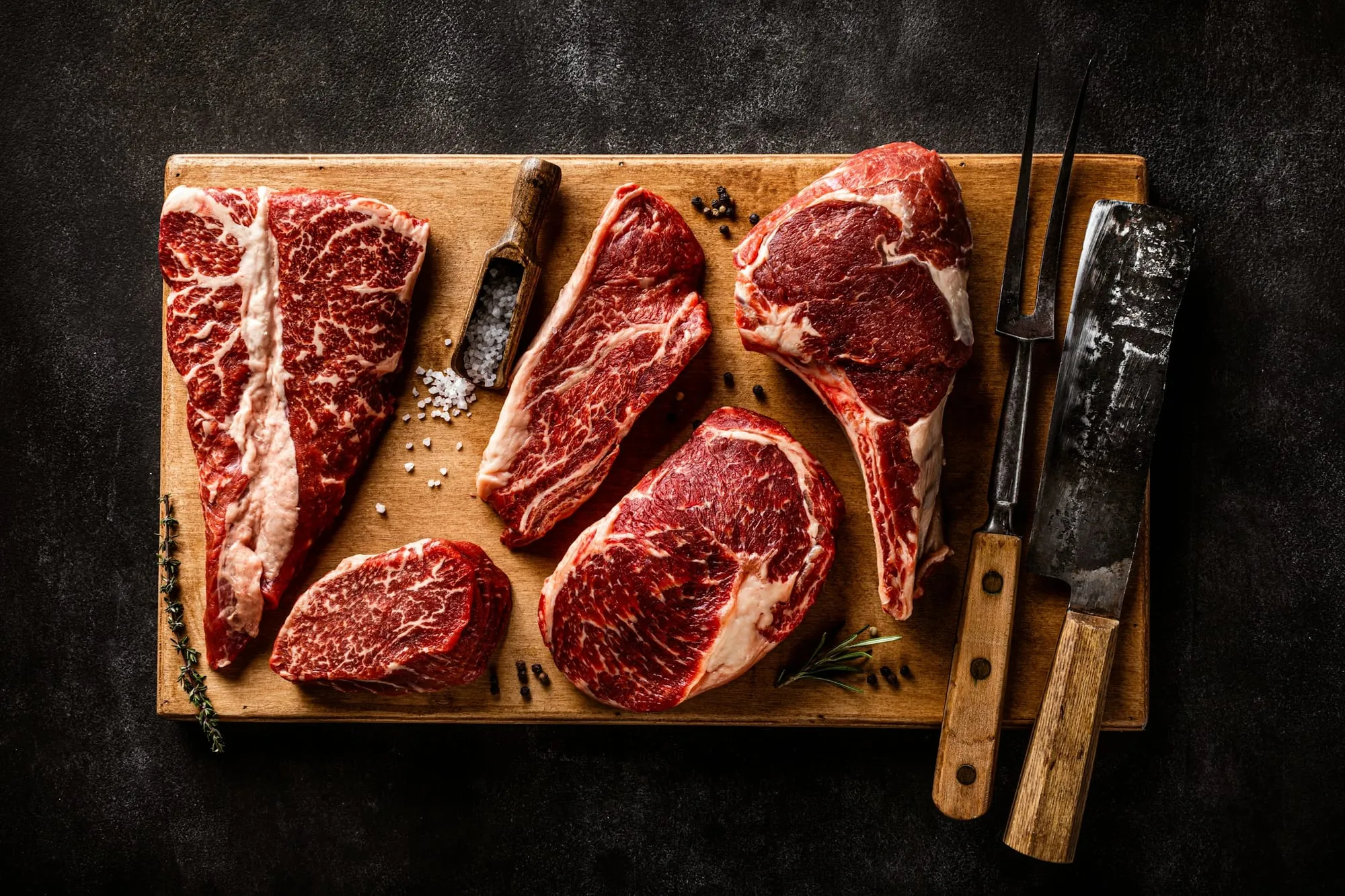 Marbled raw steaks, a tomahawk and a tenderloin on a wooden board with salt and knives (stock photo)
