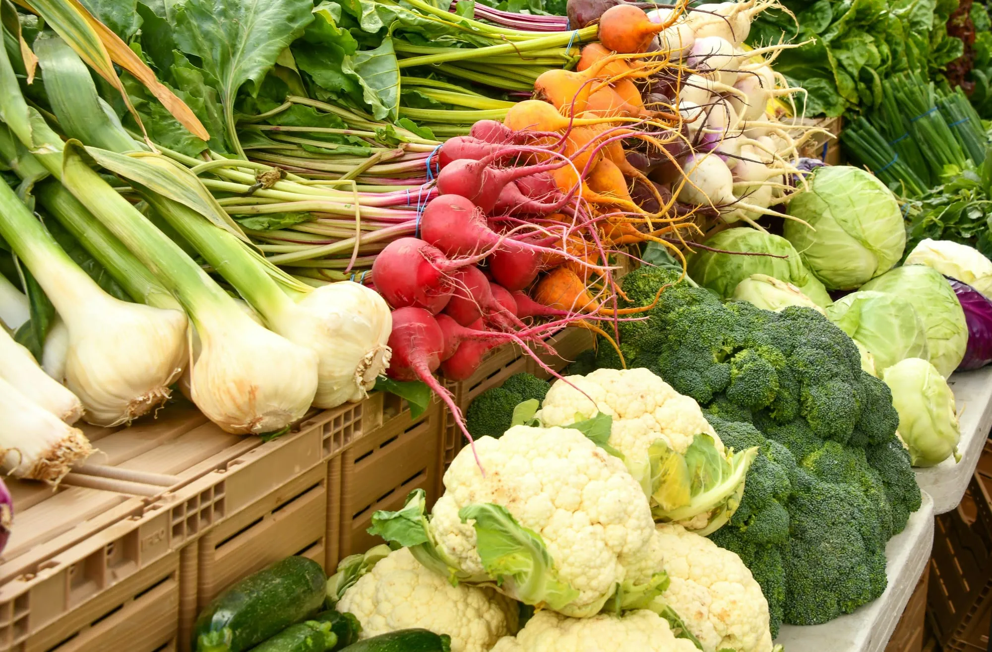 Cauliflower, broccoli, radishes, carrots and spring onions stacked on a market stall (stock photo)