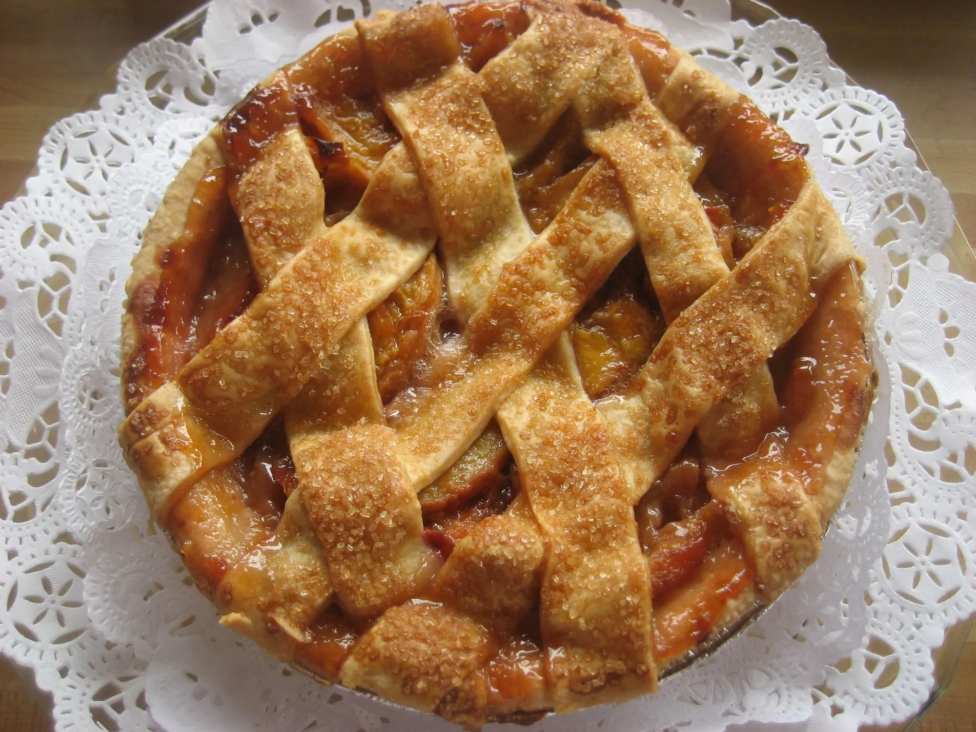 A golden lattice-top peach pie sprinkled with coarse sugar on a lace doily