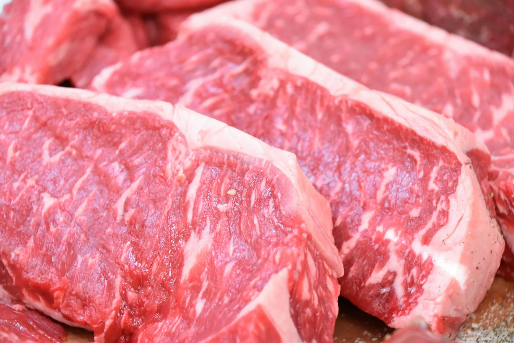 Close-up of thick, richly marbled raw strip steaks lined up side by side on a butcher block (stock photo)