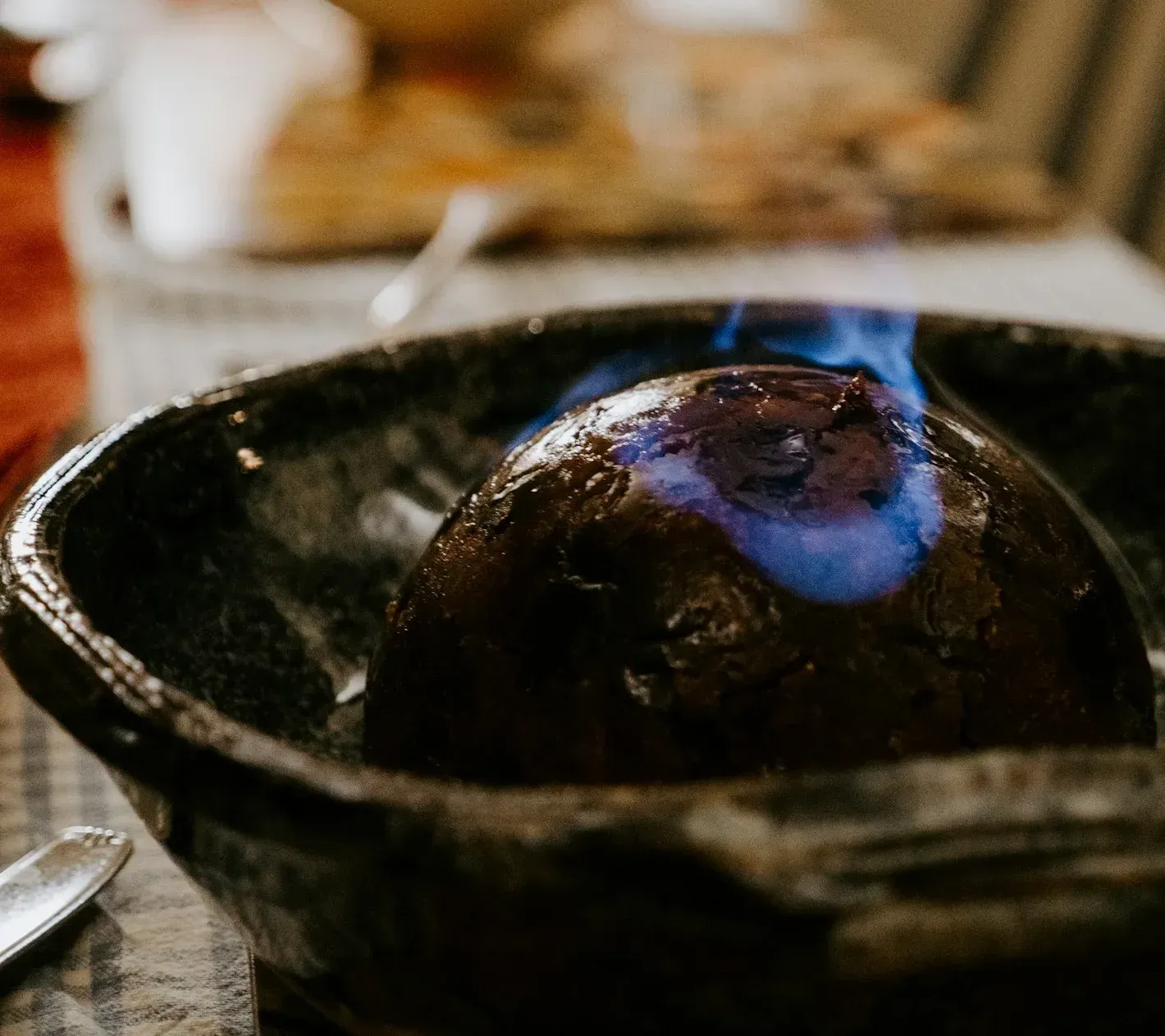 A Christmas pudding in a dark bowl, blue brandy flames licking over it