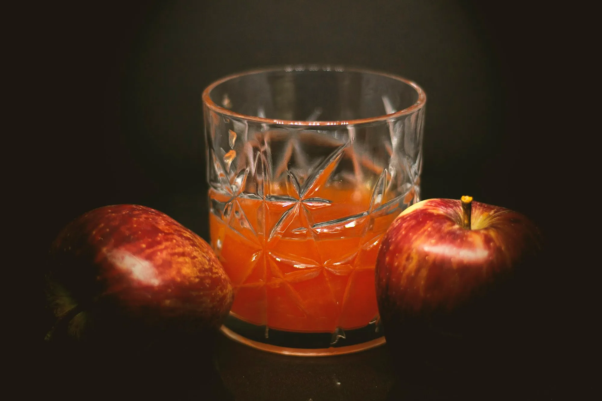 A cut crystal glass of apple cider between two red apples (stock photo)