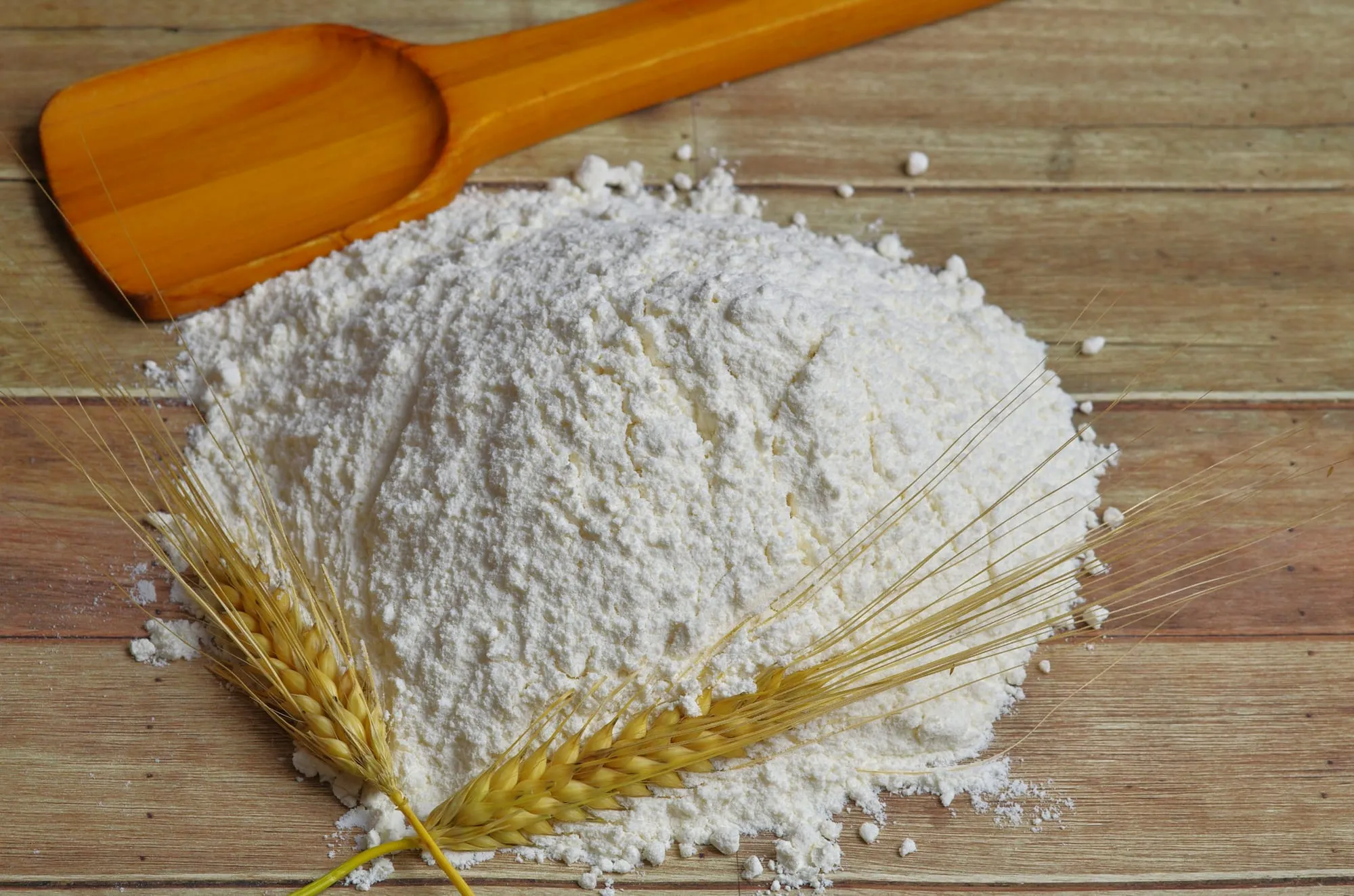 A mound of fresh flour with ears of wheat on a wooden table (stock photo)