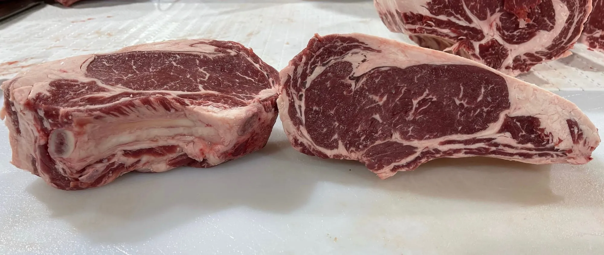 Thick-cut, well-marbled grass-fed ribeye steaks on a butcher block