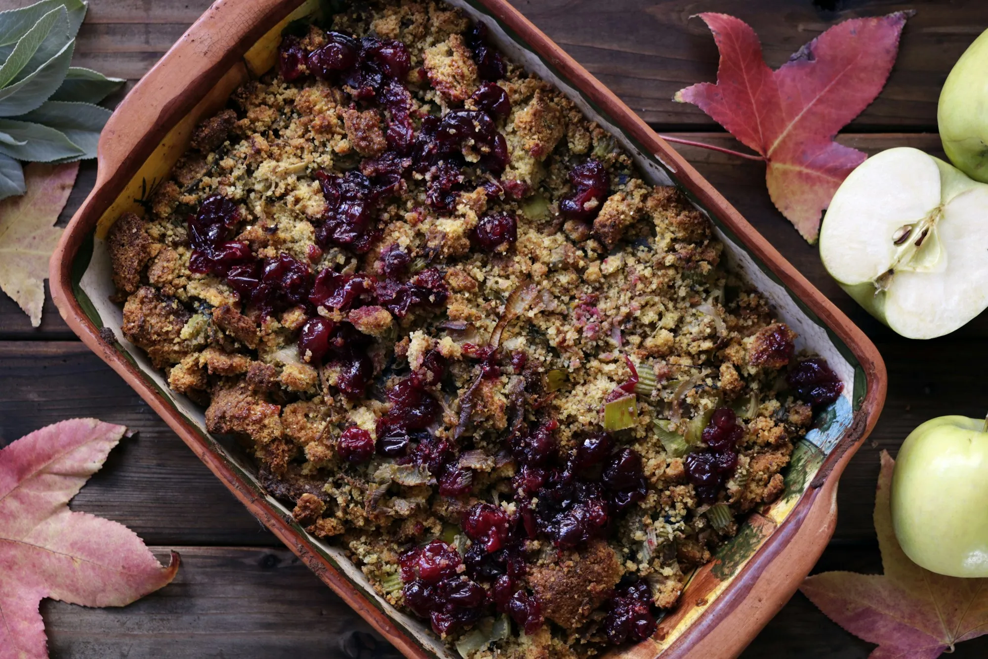 A baking dish of golden bread stuffing studded with dried cranberries, with apples and autumn leaves (stock photo)