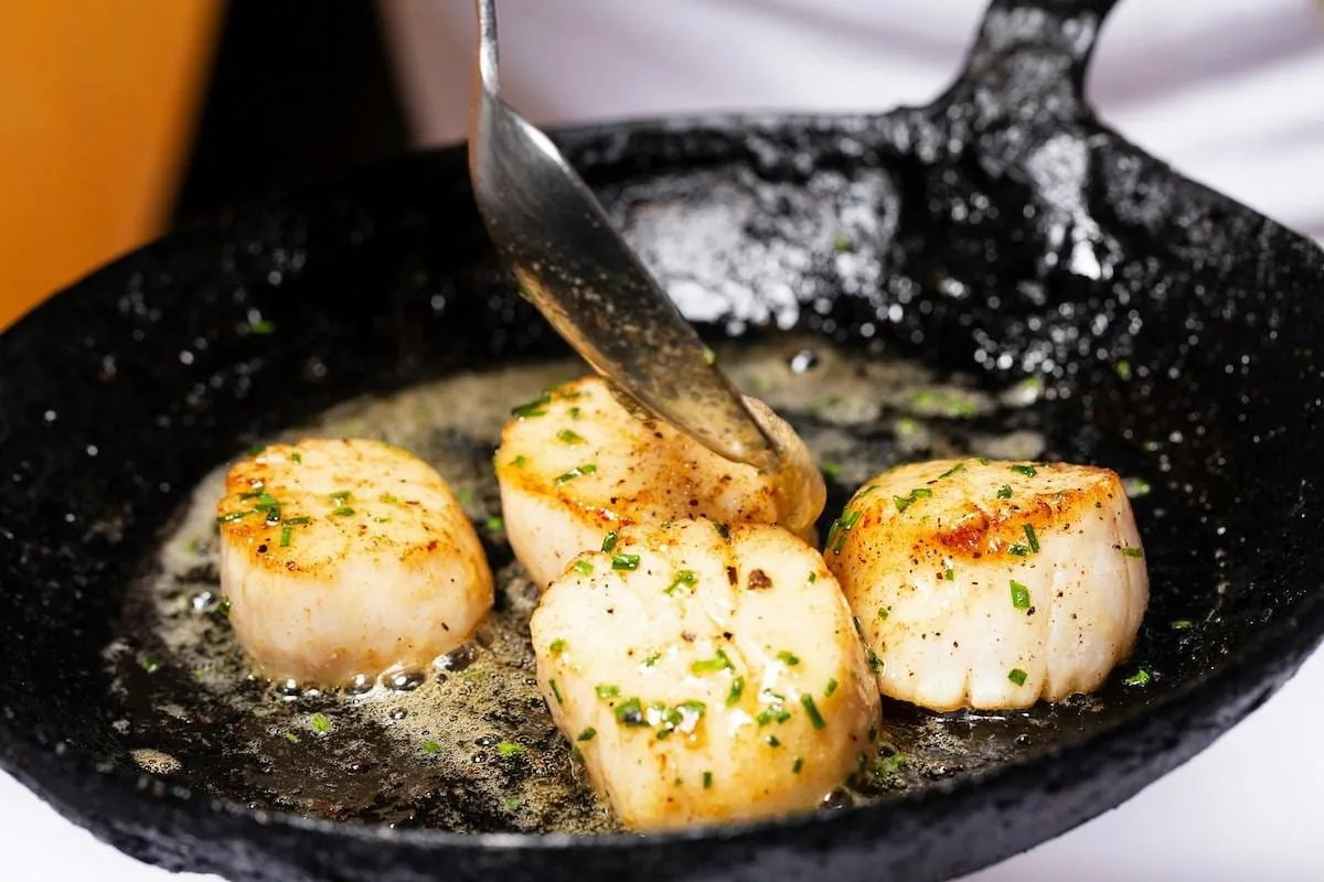 Seared sea scallops being basted with butter in a cast-iron pan