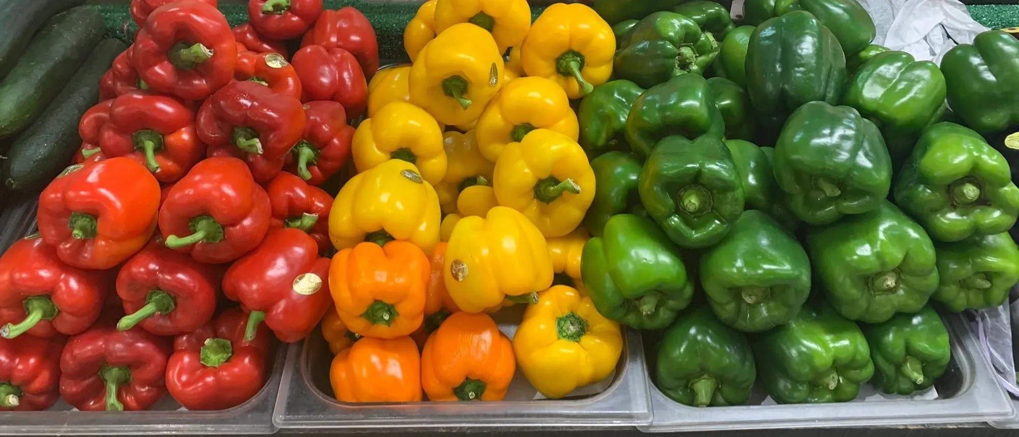 Red, yellow, orange and green bell peppers stacked in rows at the produce stand