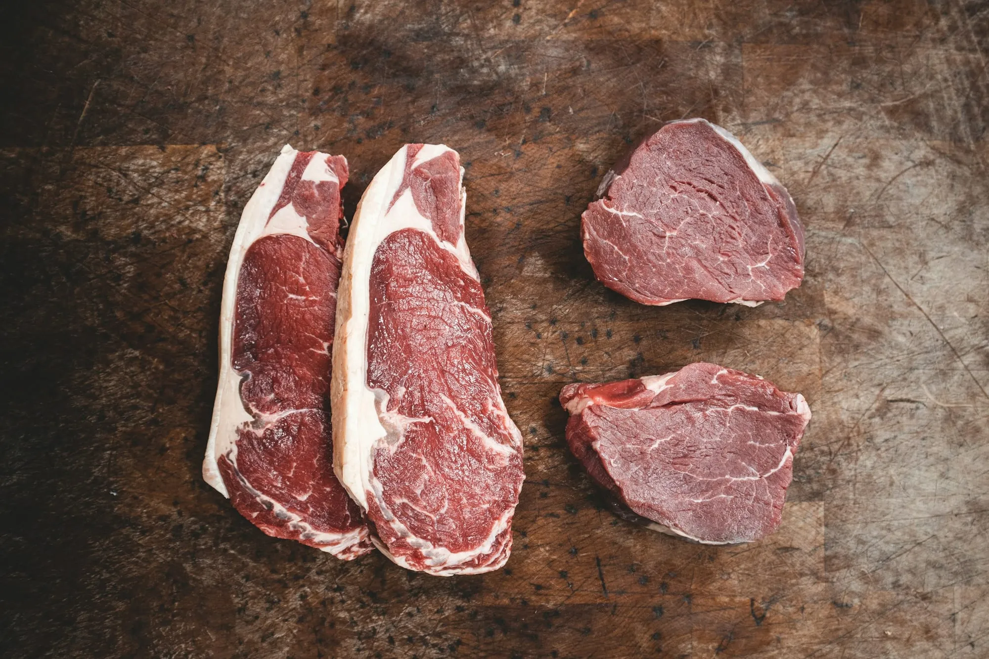 Raw sirloin and fillet steaks on a dark wooden board (stock photo)