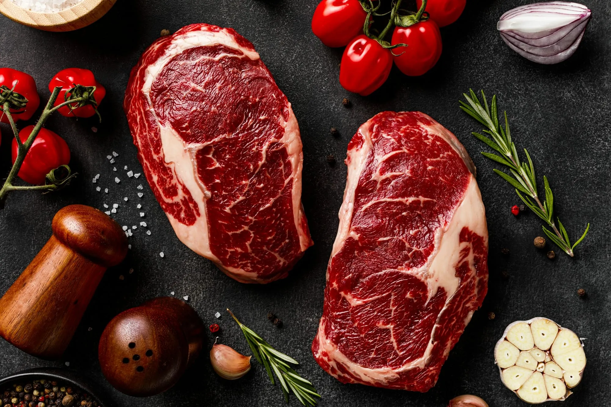 Two marbled raw ribeye steaks with rosemary, garlic and peppercorns (stock photo)