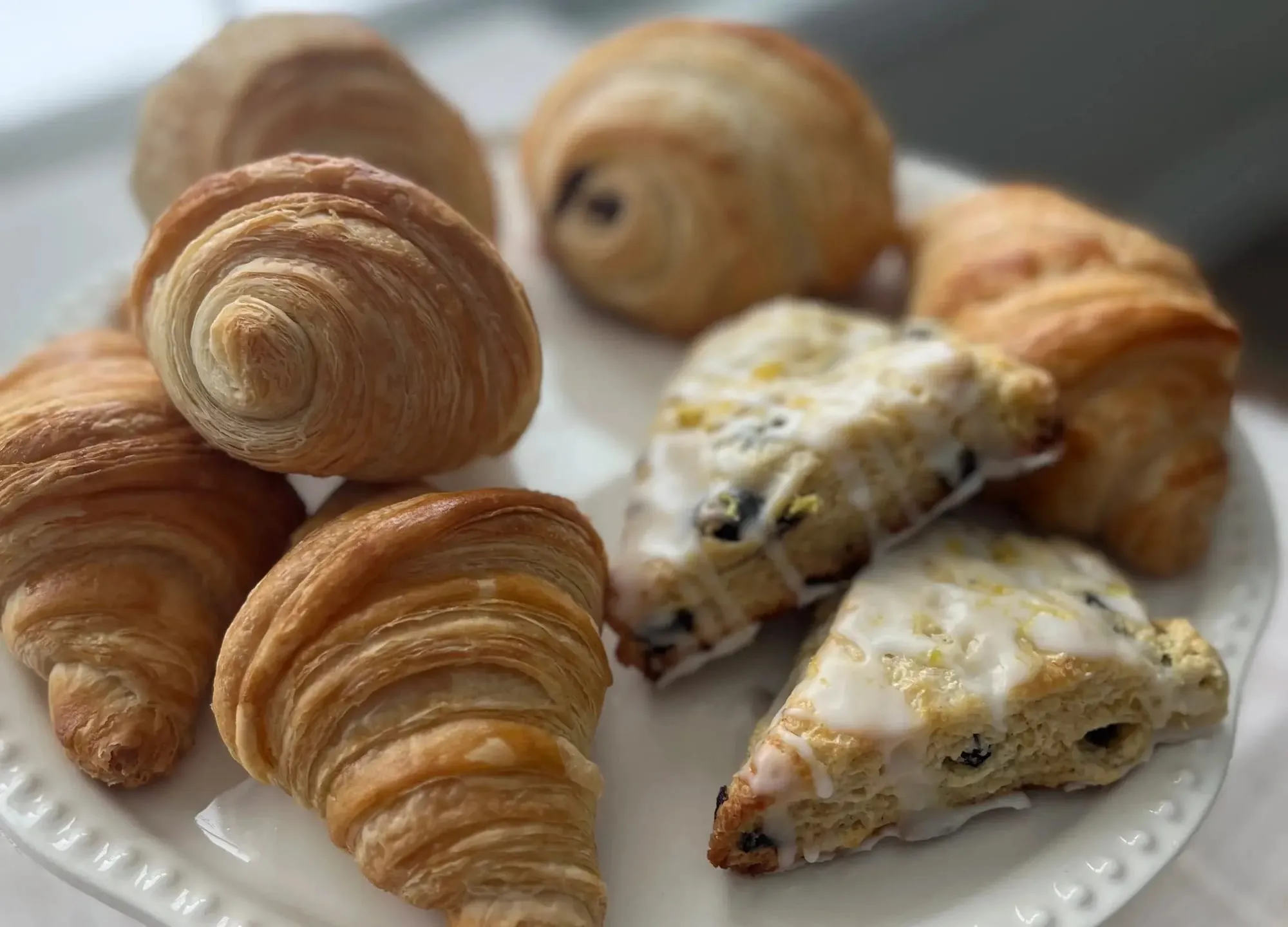 Sourdough croissants, pain au chocolat and glazed blueberry scones on a white cake stand