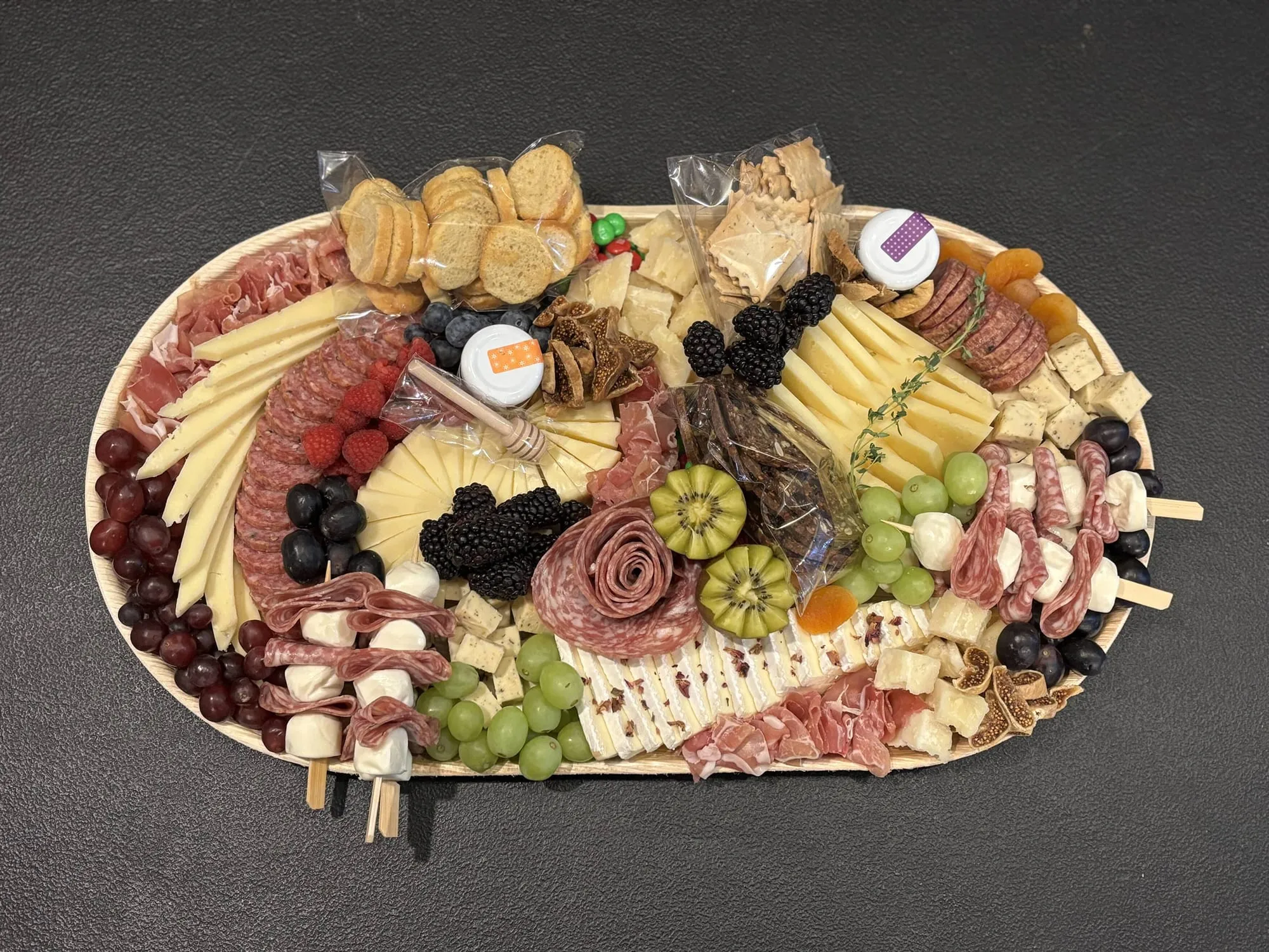 A cheese and charcuterie board with sliced cheeses, salami roses, berries, grapes, kiwi and crackers