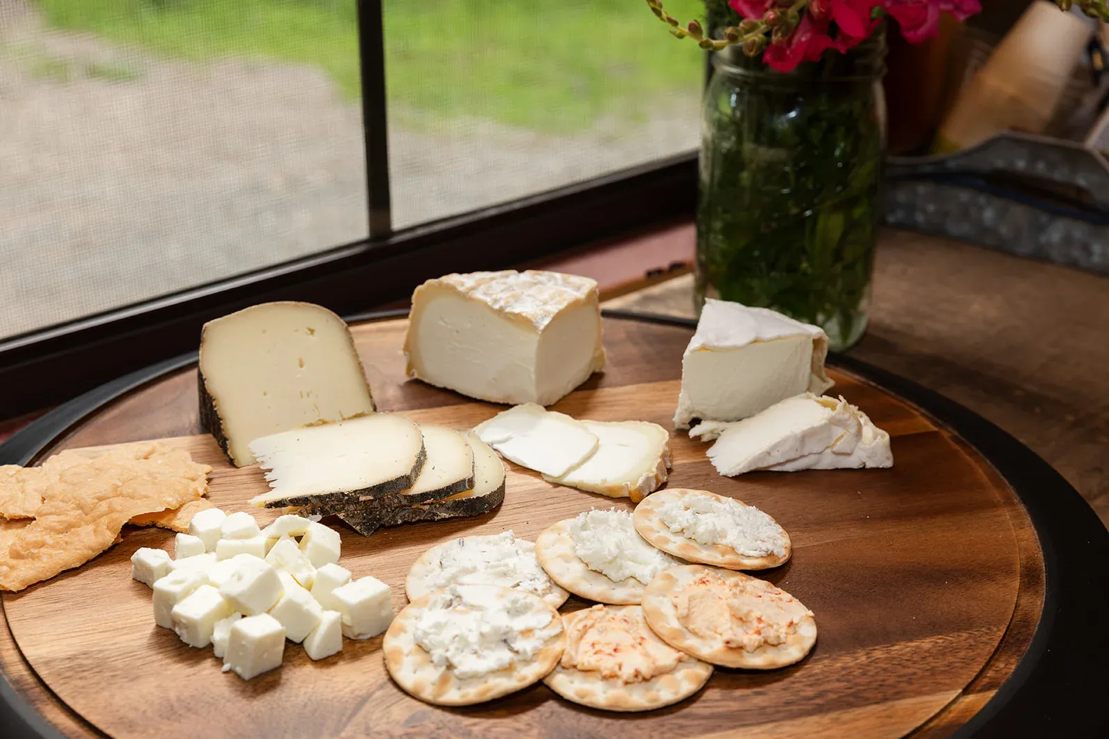 Gorgeous Goat Creamery cheeses on a wooden board: aged goat Gouda, soft-ripened wedges, feta cubes and chèvre spread on crackers