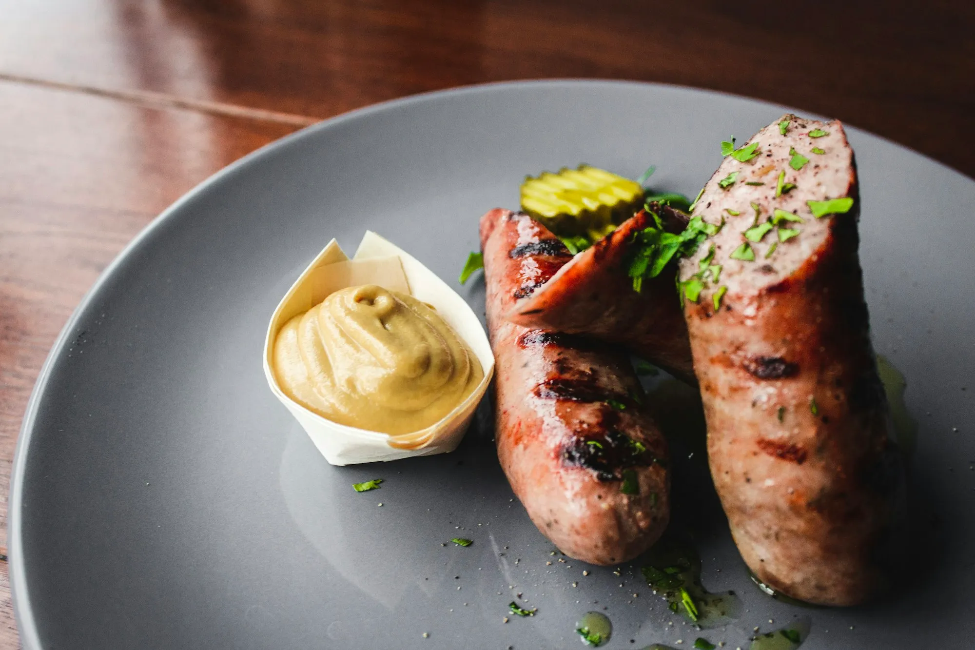Grilled pork sausages, one cut open, with a cup of mustard and fresh herbs (stock photo)