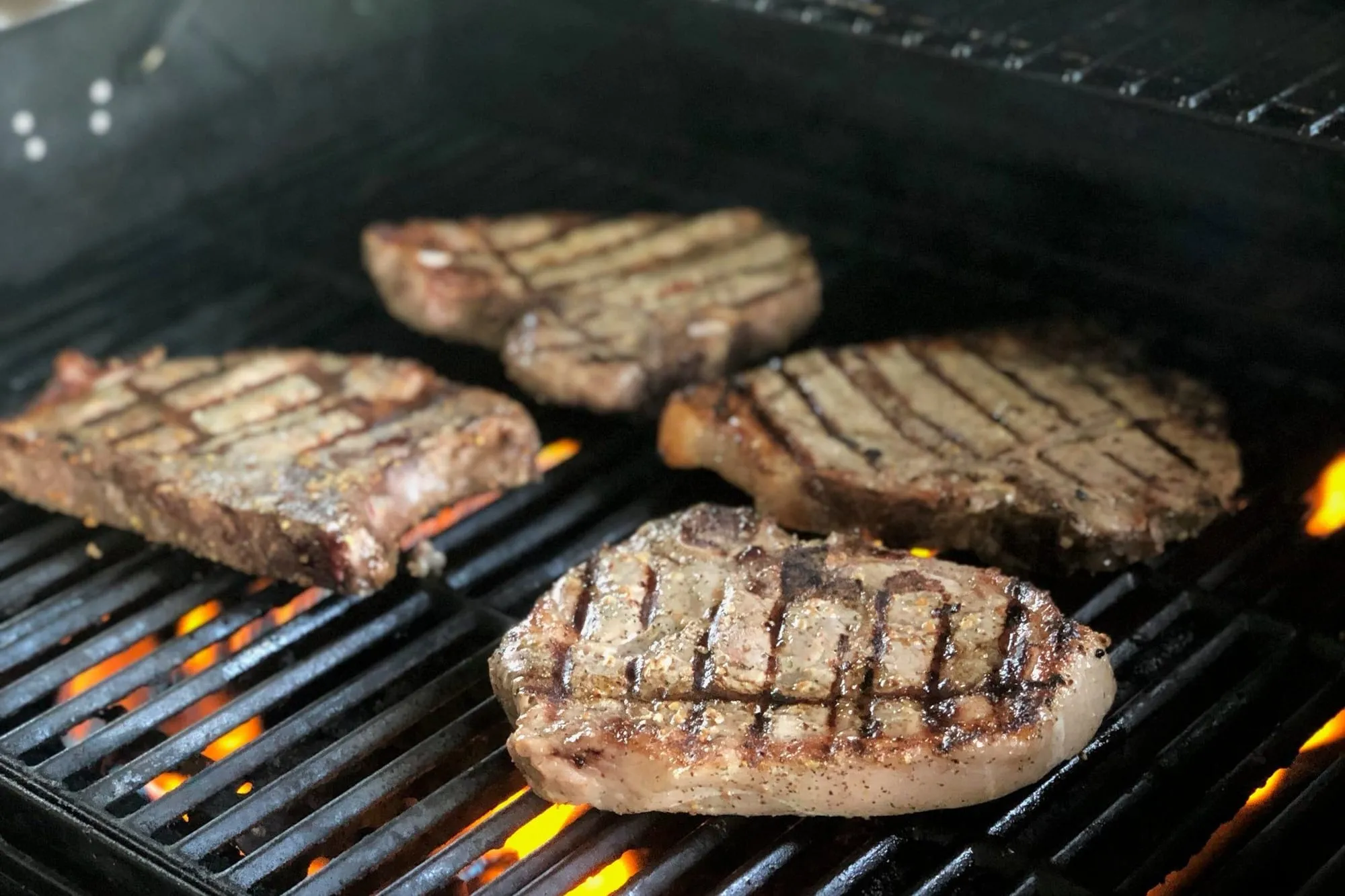 Thick-cut pasture-raised chops searing over open flames on a grill
