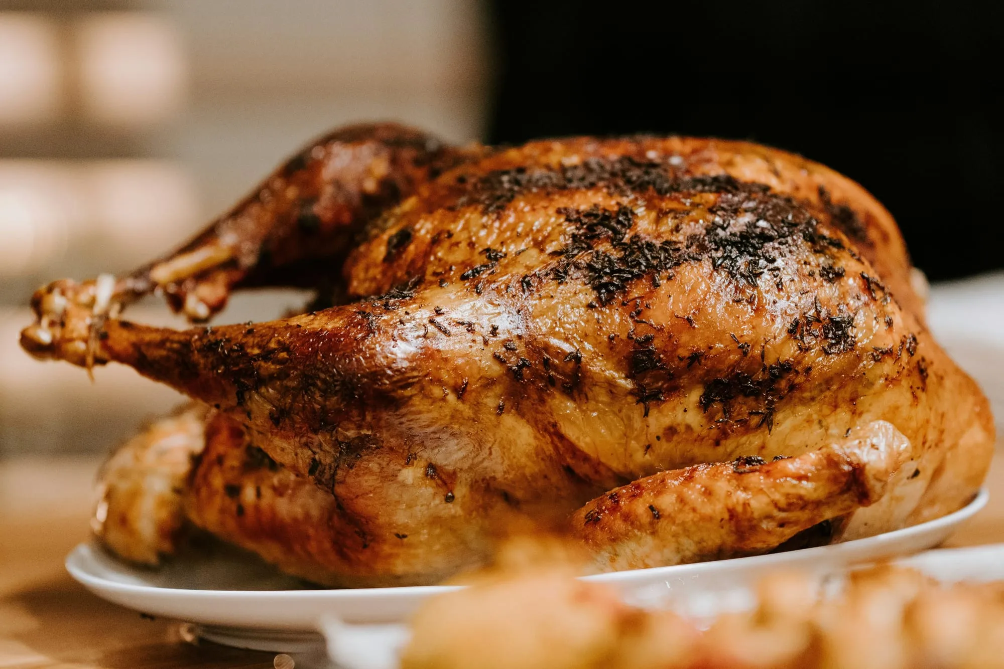 A golden roast chicken with crisp, herb-flecked skin on a white plate (stock photo)