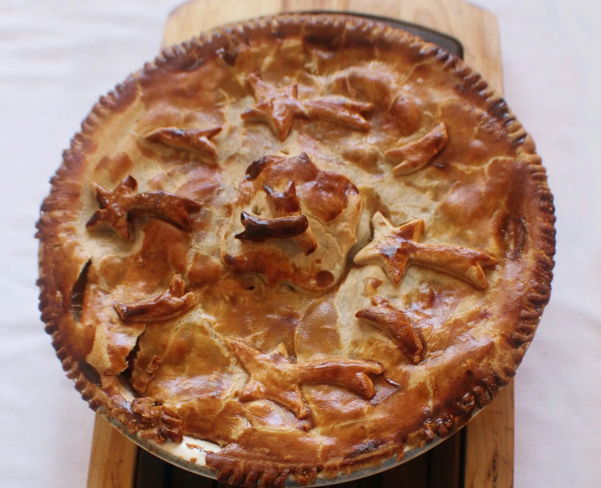 A golden double-crust pie decorated with pastry cutouts on a wooden board (stock photo)