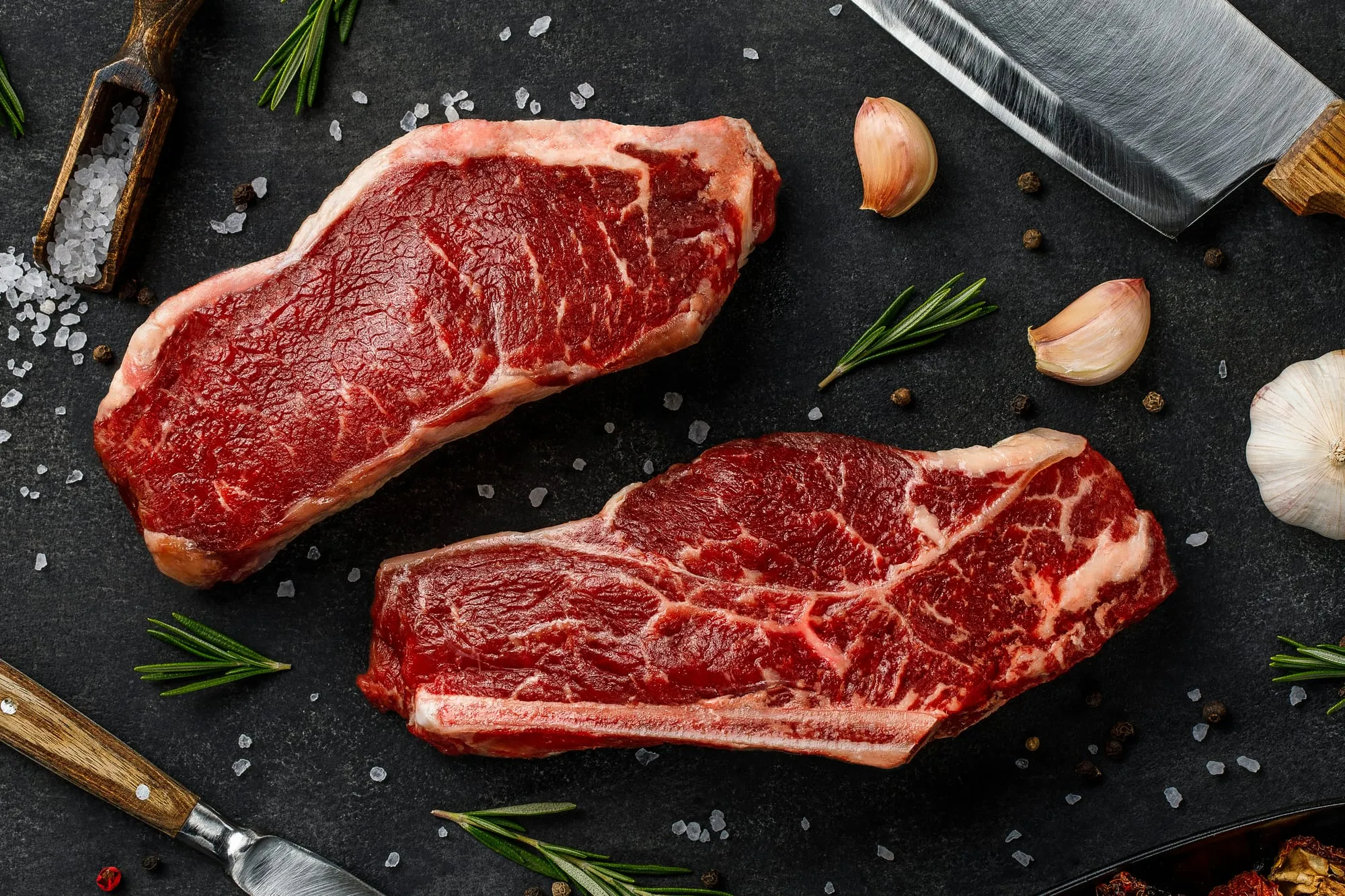 Two well-marbled raw strip steaks with herbs, garlic and salt (stock photo)