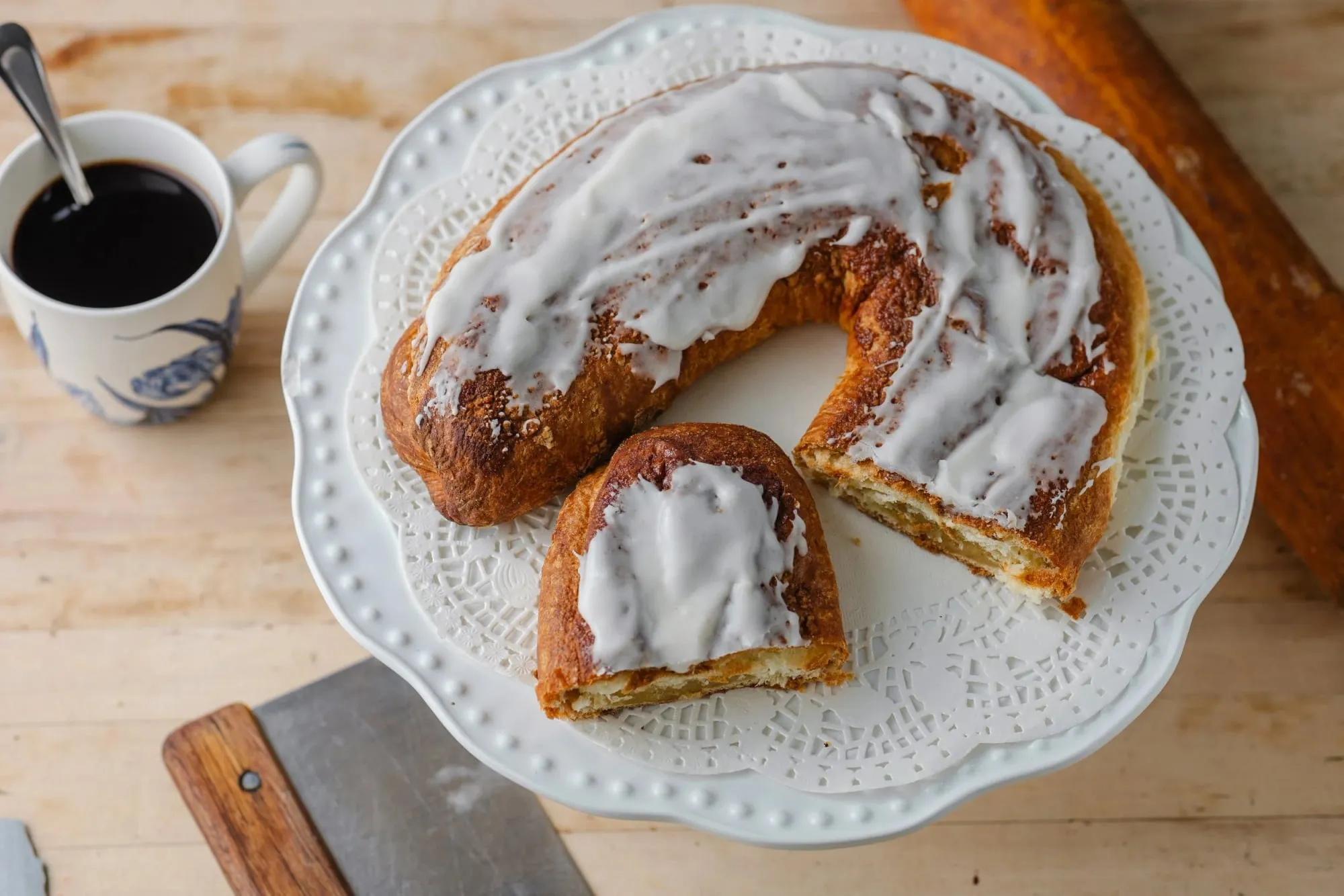 An iced, almond-filled Dutch ring loaf, sliced, with a cup of coffee at Holland American Bakery