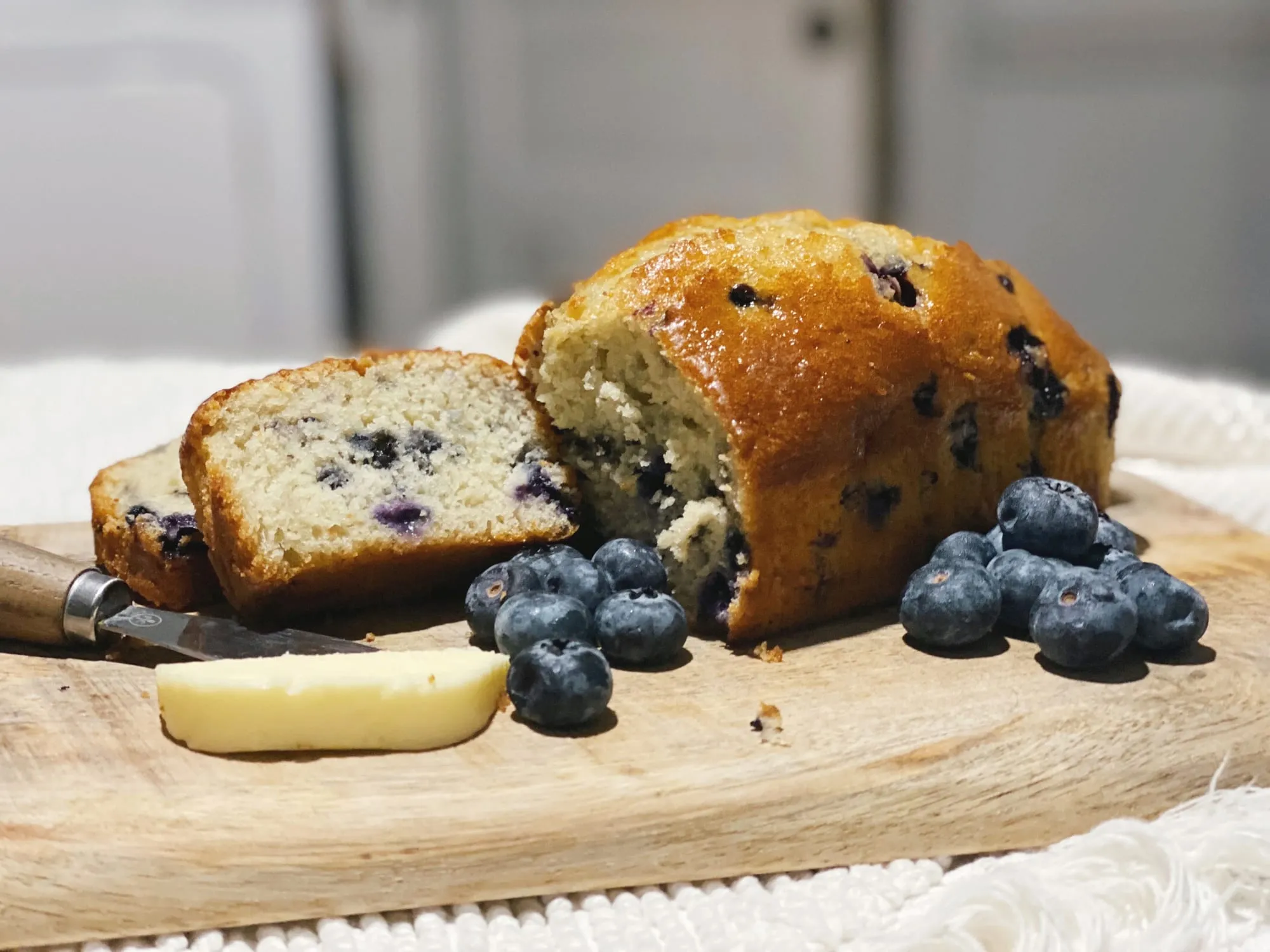 A sliced blueberry tea bread with fresh blueberries on a wooden board