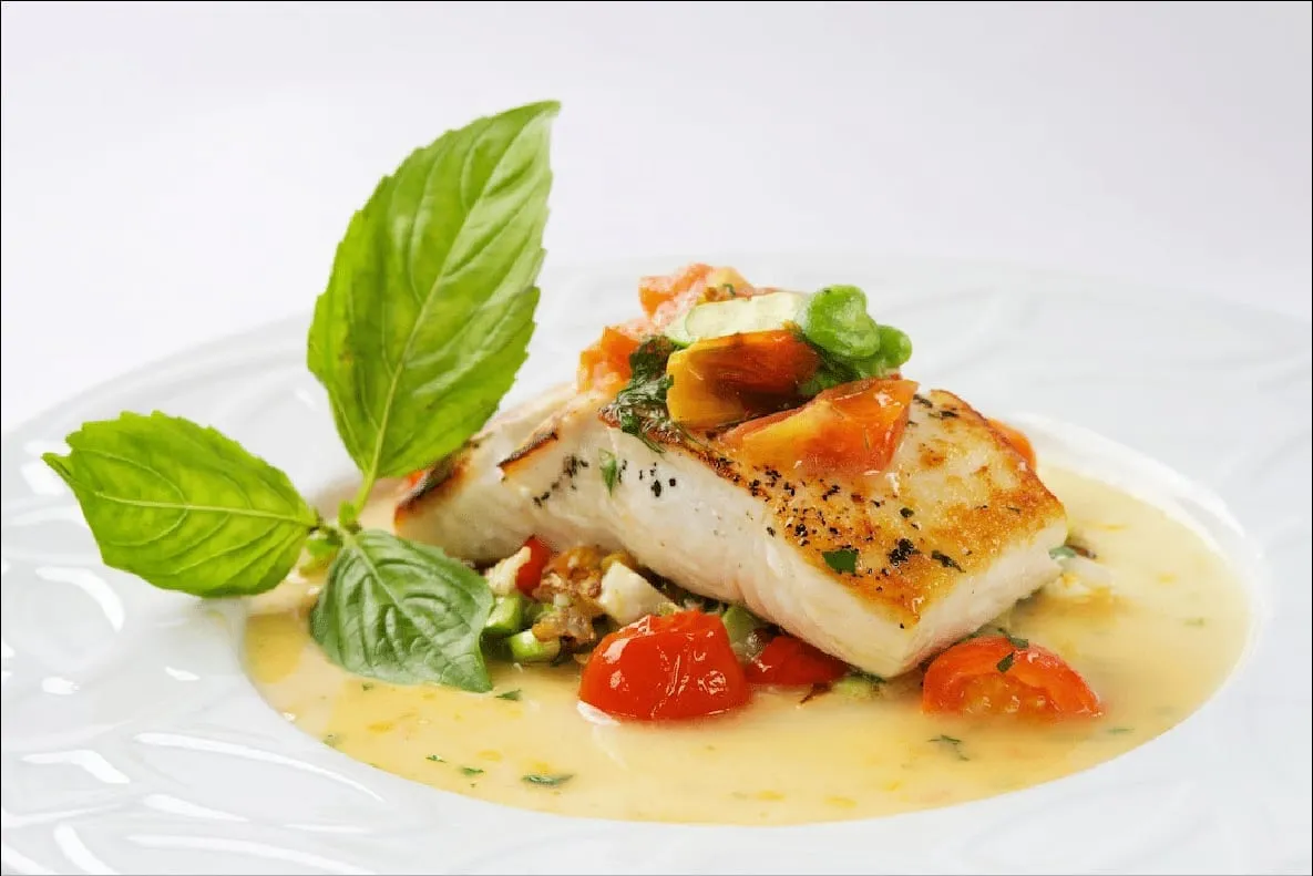 Seared white fish in a light sauce with cherry tomatoes and fresh basil on a white plate