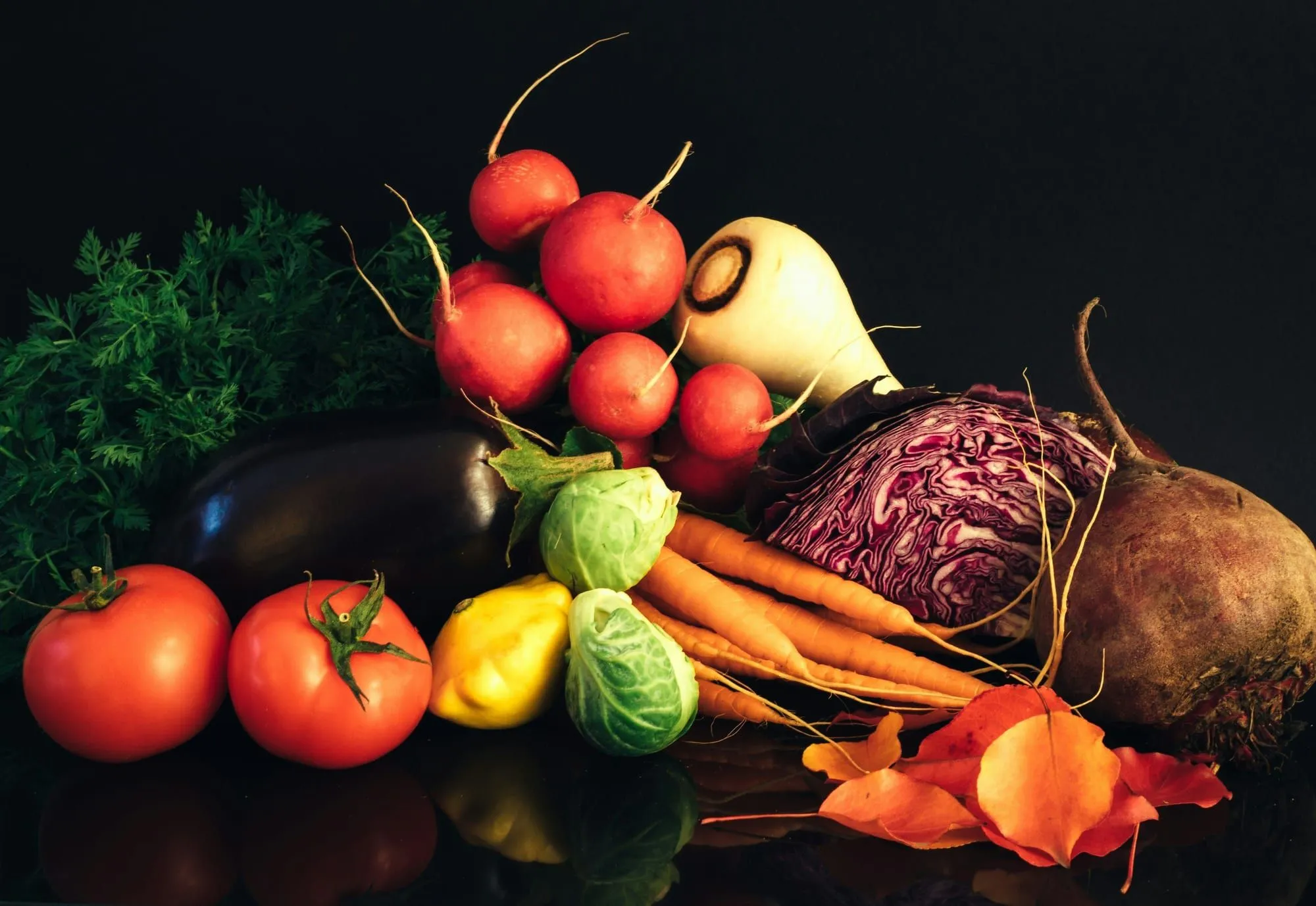 Radishes, tomatoes, carrots, beets, red cabbage, Brussels sprouts and parsnip against a black background (stock photo)