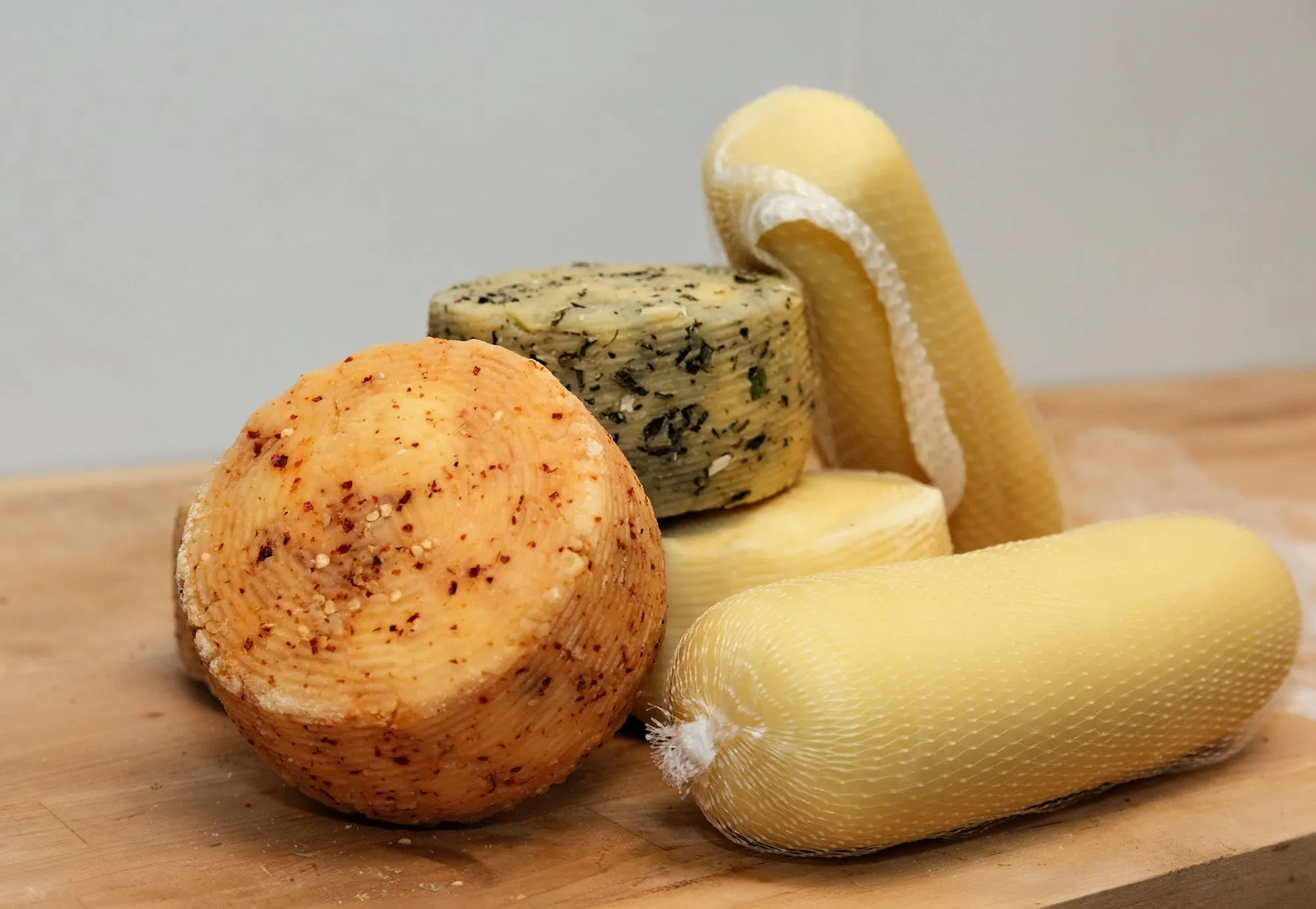 Aged primo sale wheels, one rubbed with chili and one with herbs, beside netted scamorza on a wooden board