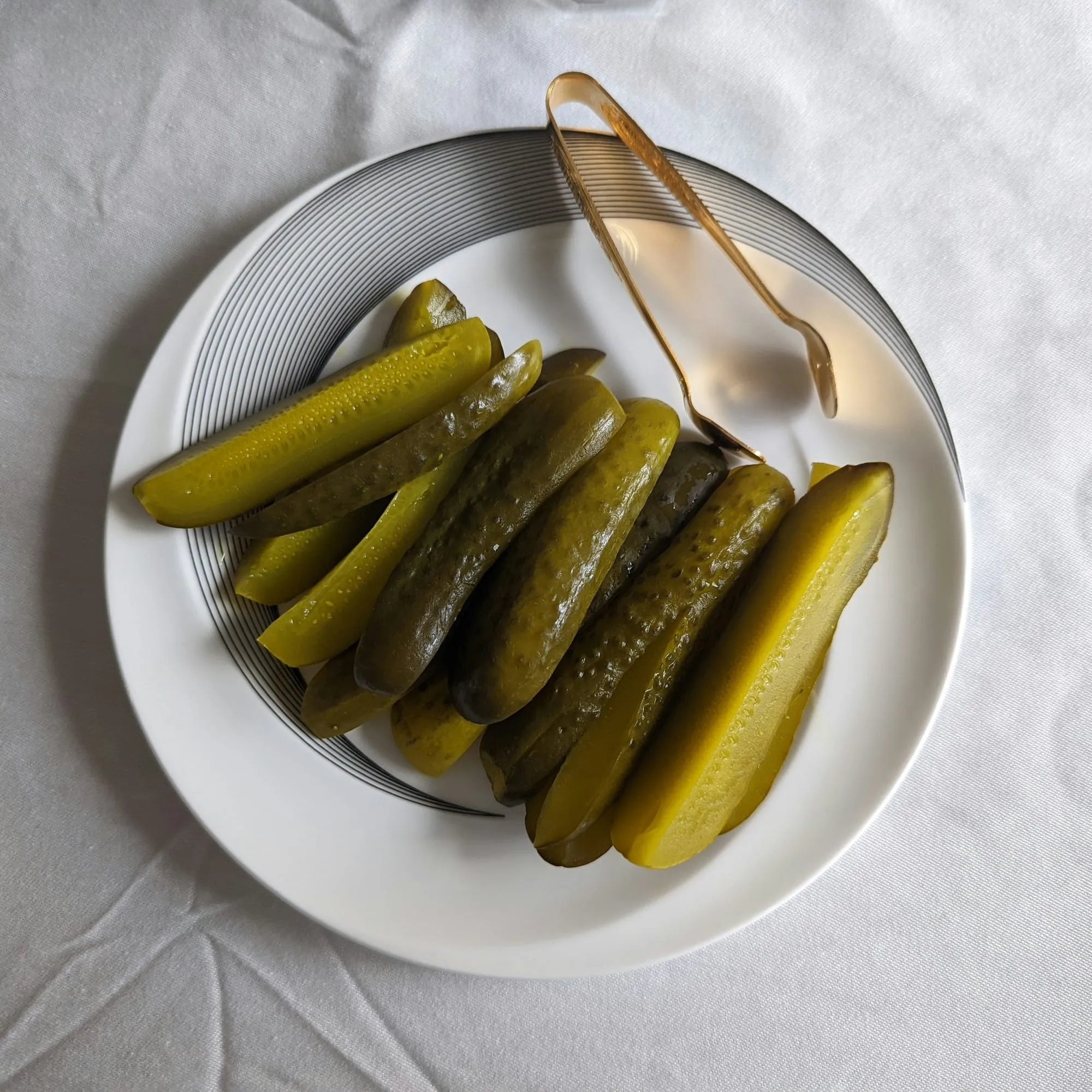 Dill pickle spears on a white plate with brass serving tongs