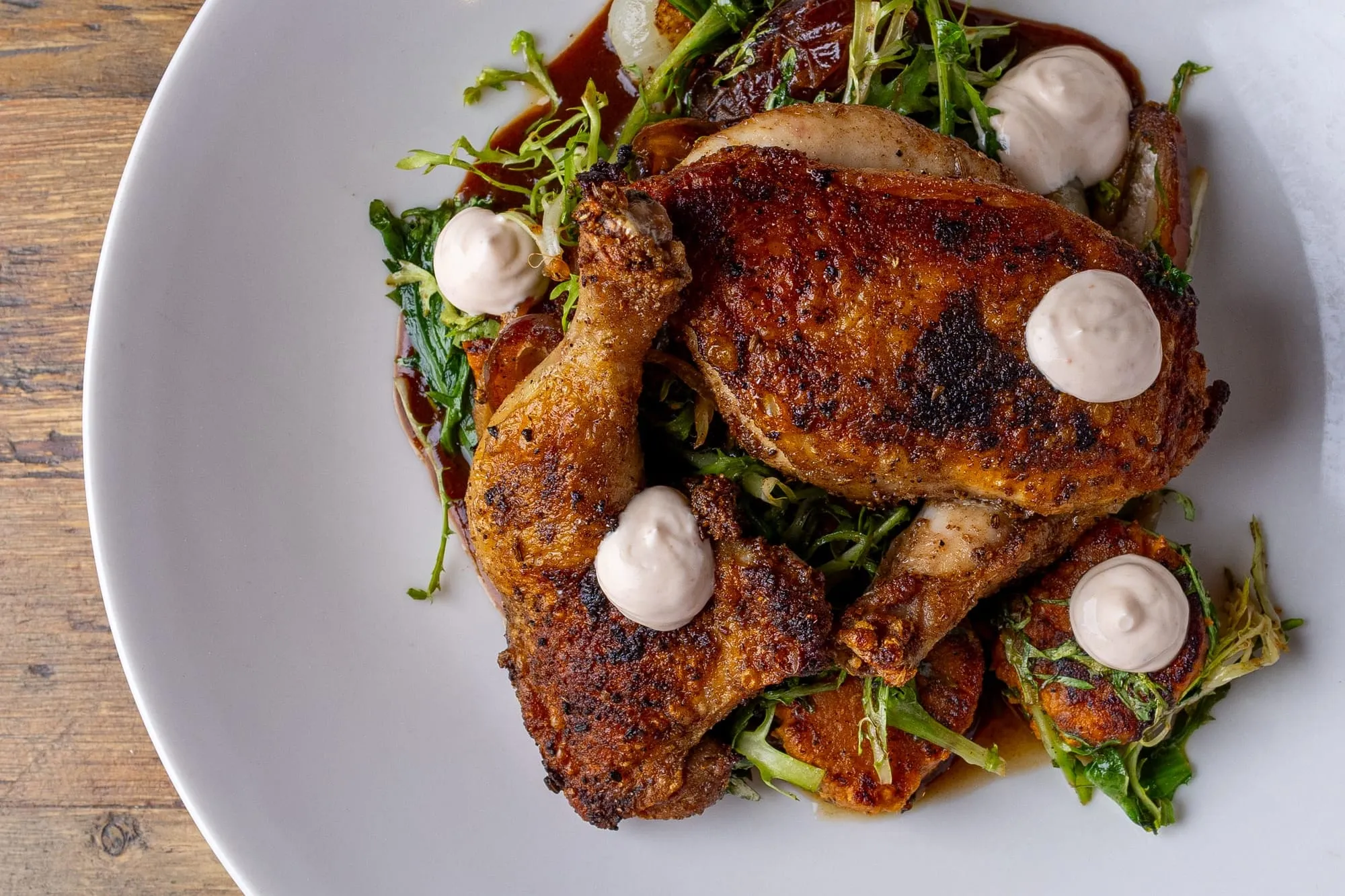 A spice-rubbed roast half chicken over greens with dollops of sauce on a white plate