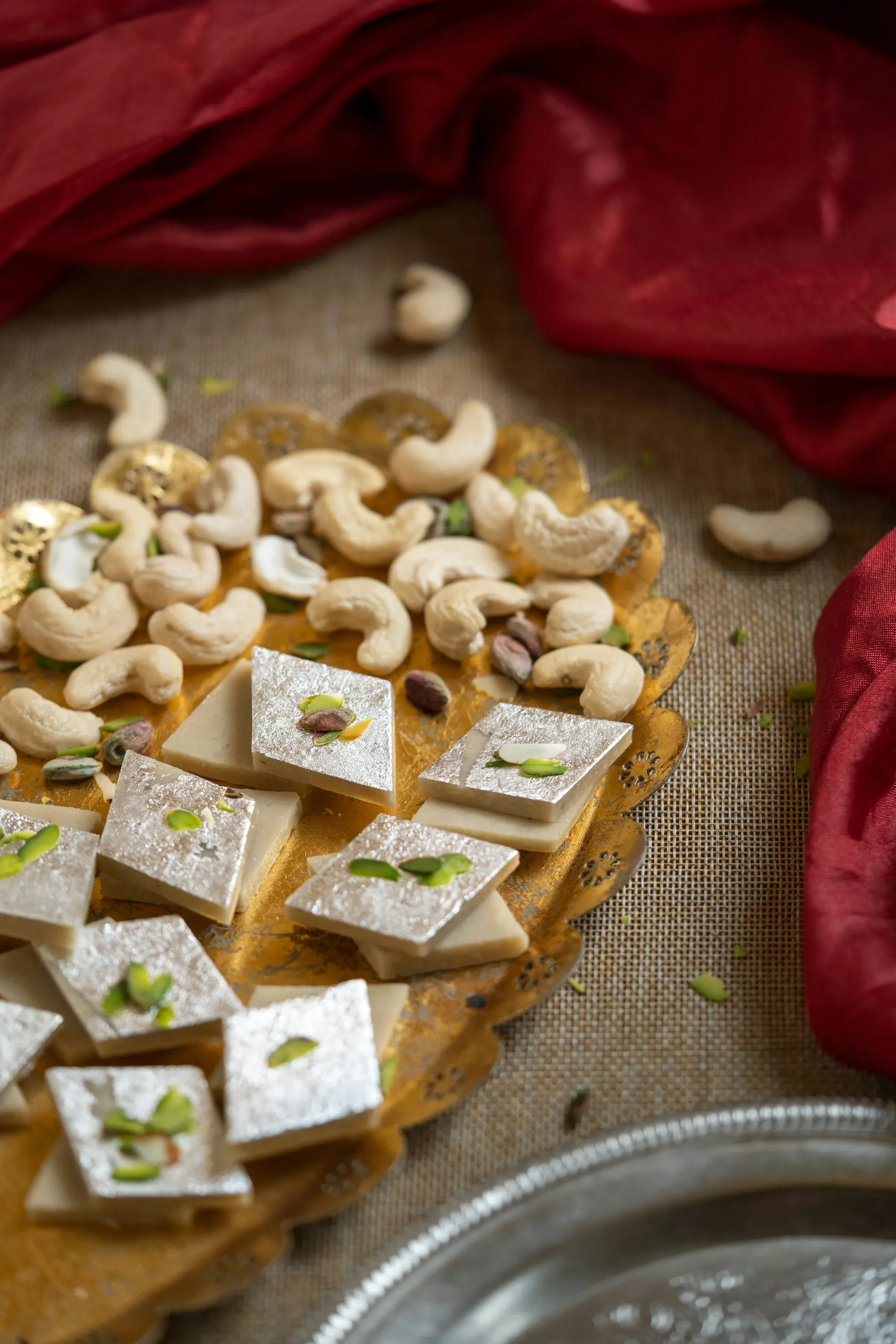 Diamond-shaped kaju katli topped with silver leaf on a plate with cashews