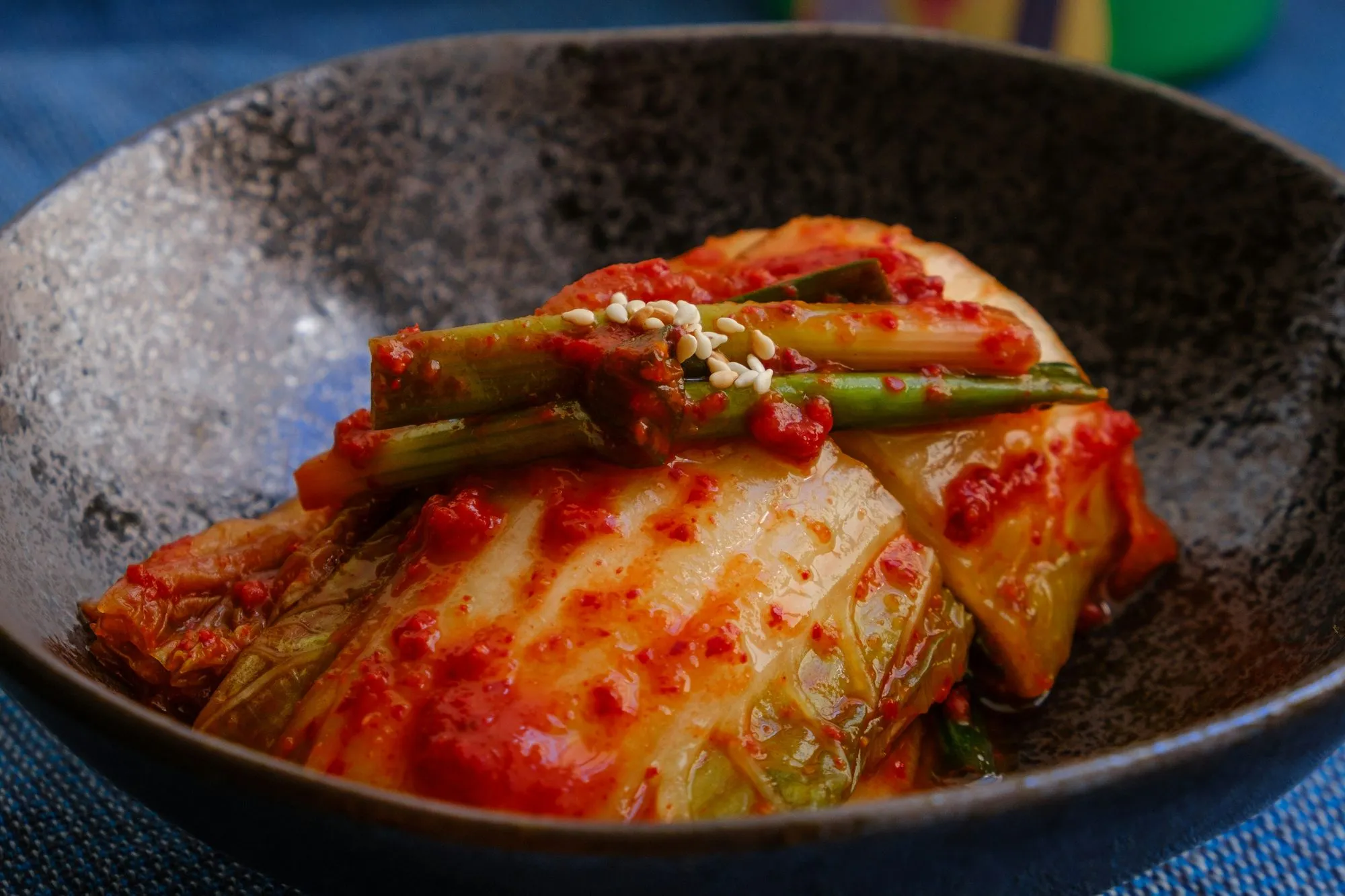 Napa cabbage kimchi with scallions and sesame seeds in a dark stoneware bowl