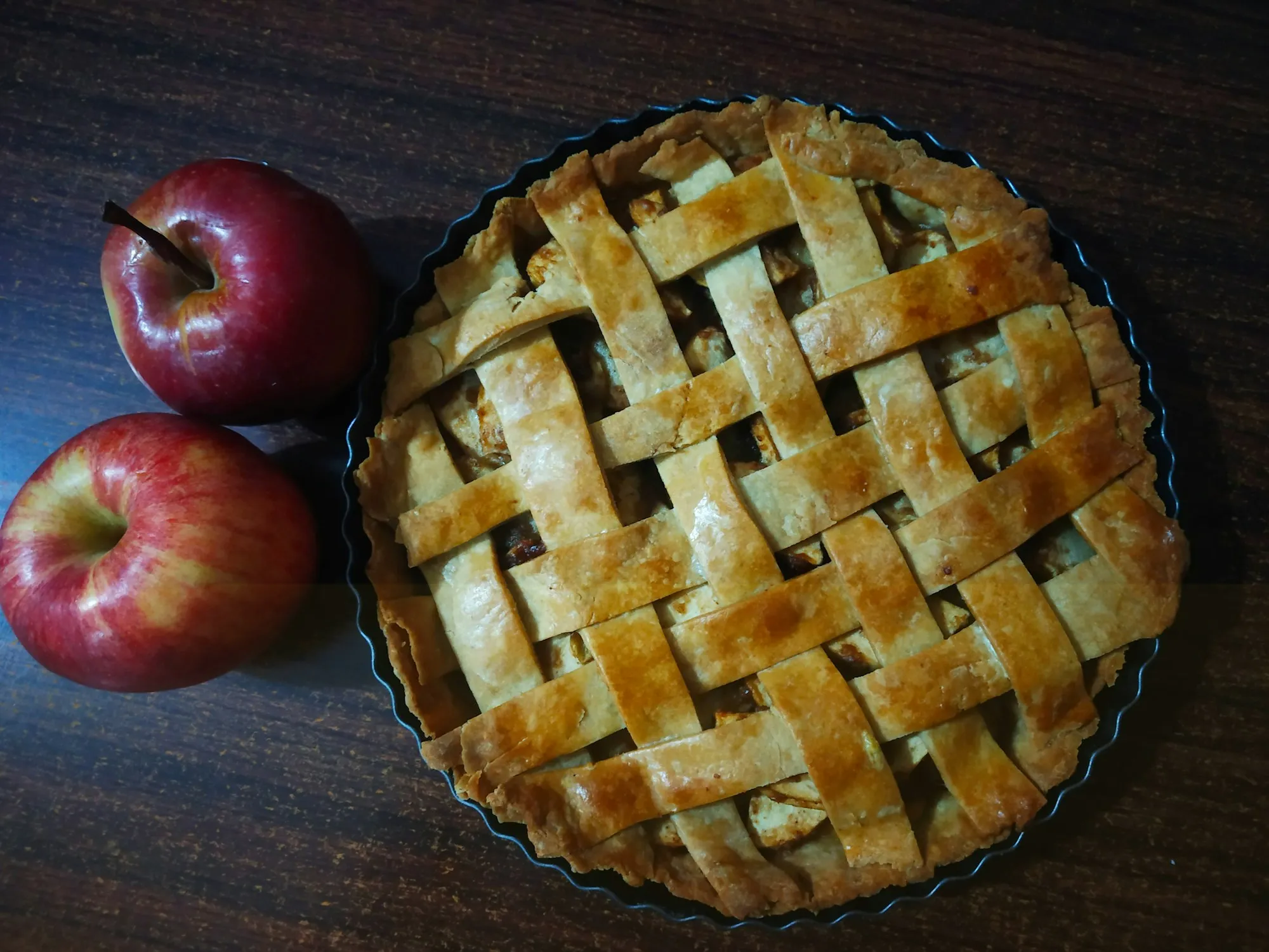 A golden lattice-top apple pie beside two red apples (stock photo)