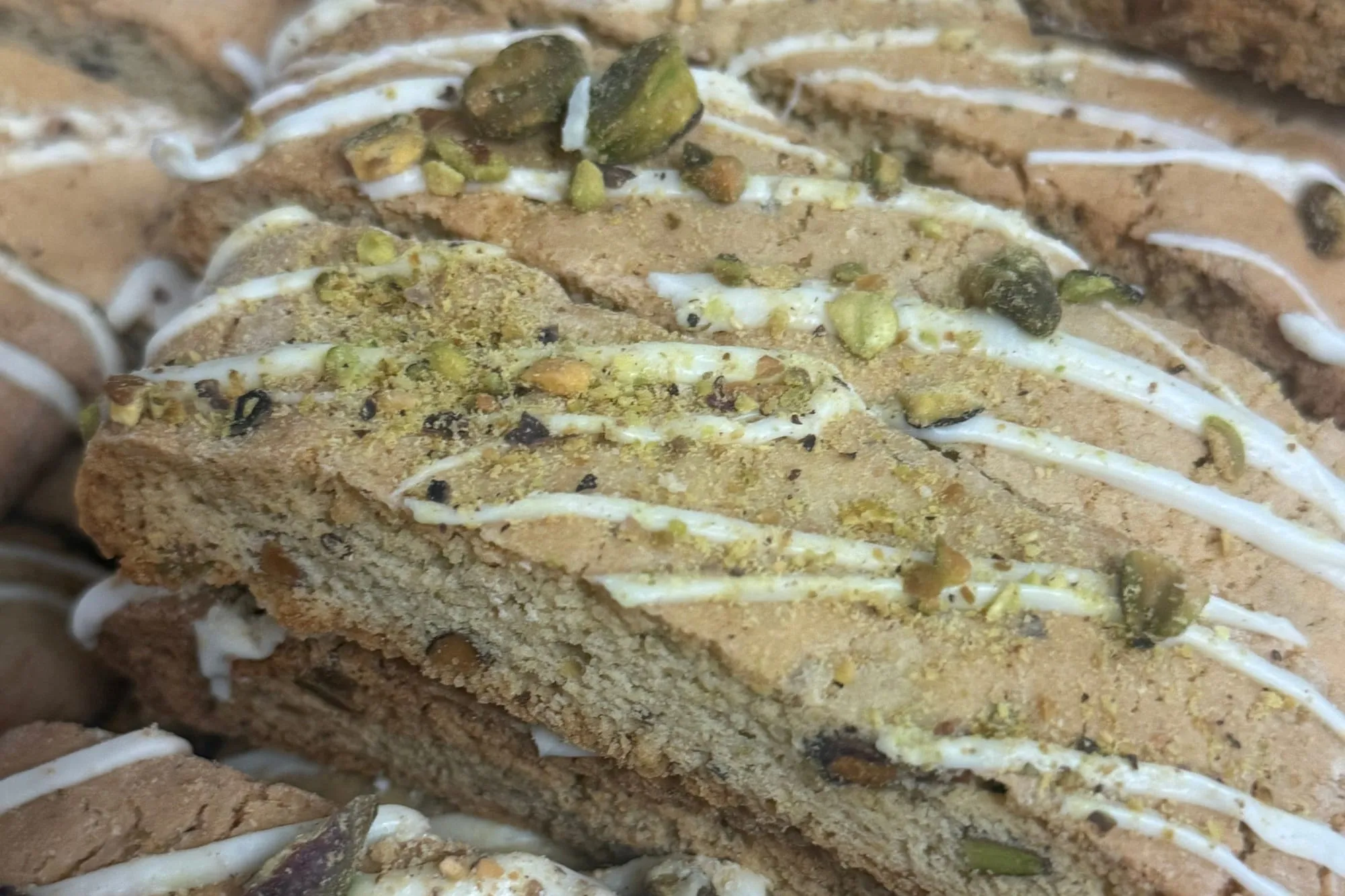 Pistachio biscotti drizzled with white icing and topped with chopped pistachios