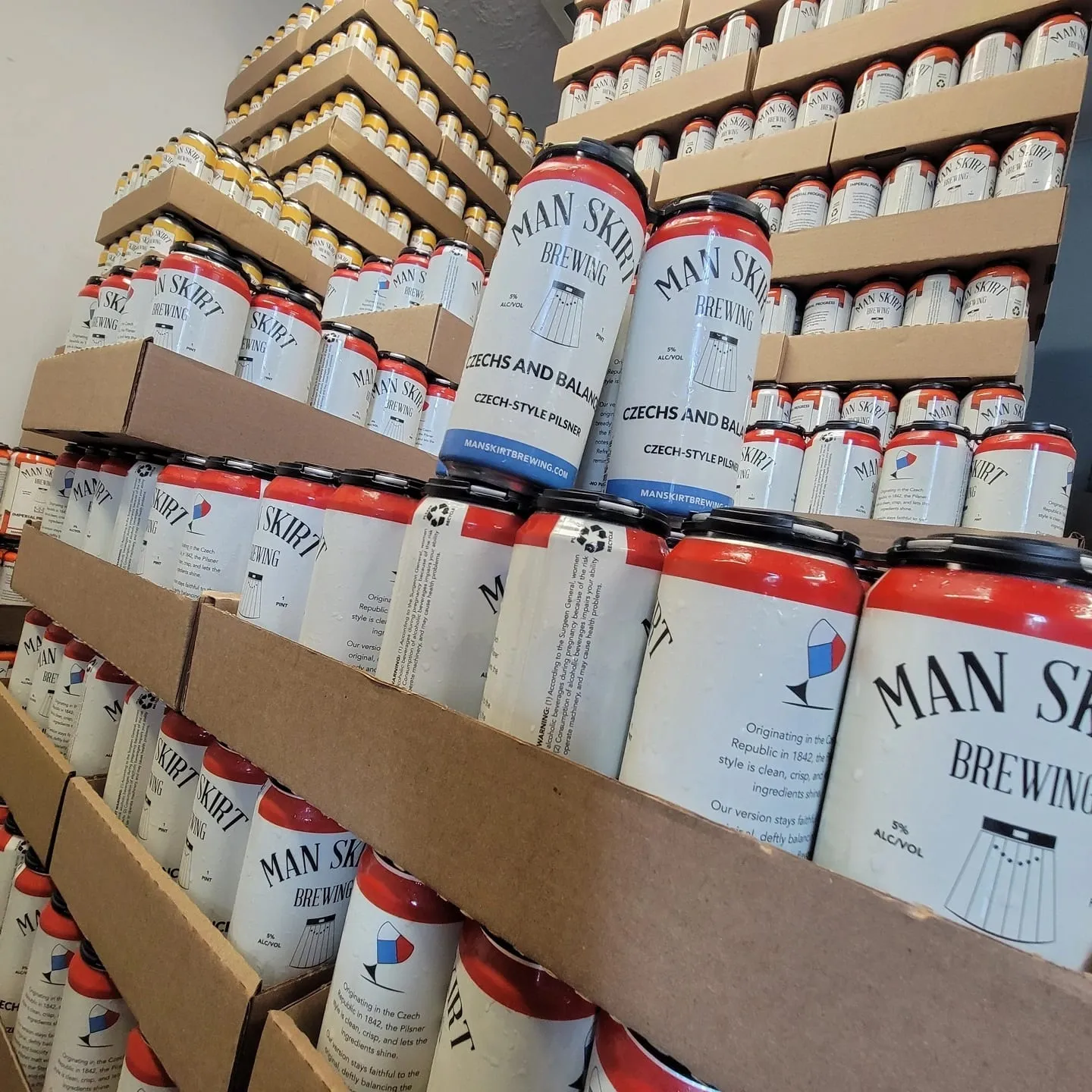 Cases of Man Skirt Brewing cans stacked on shelves