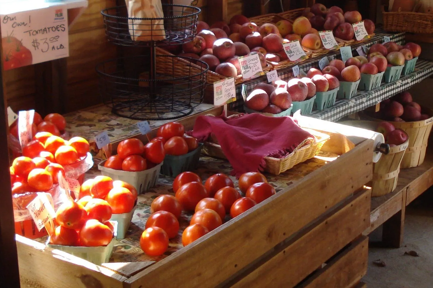 Ripe tomatoes in quart baskets and red apples on the shelves of the farm shop