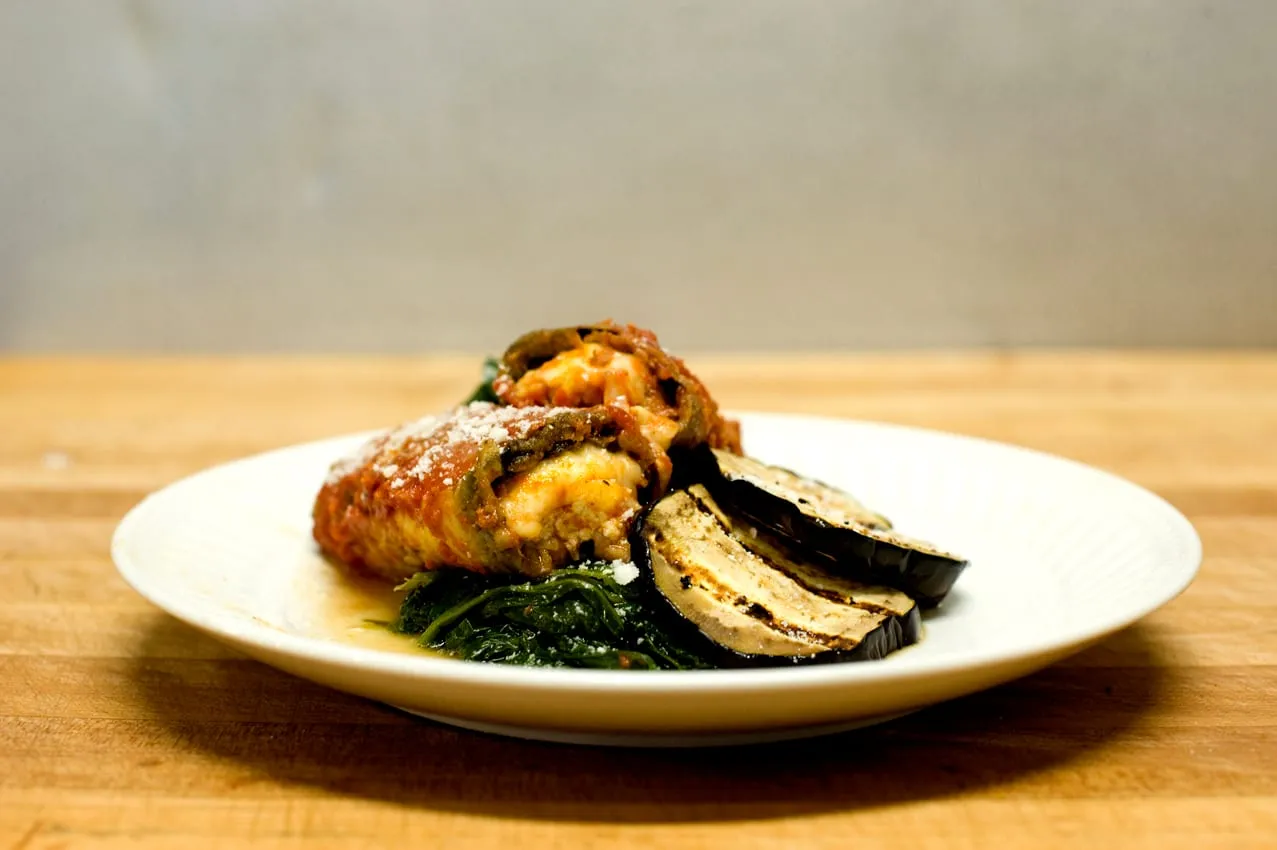 A stuffed, cheese-filled roll in tomato sauce with grilled eggplant and sauteed greens