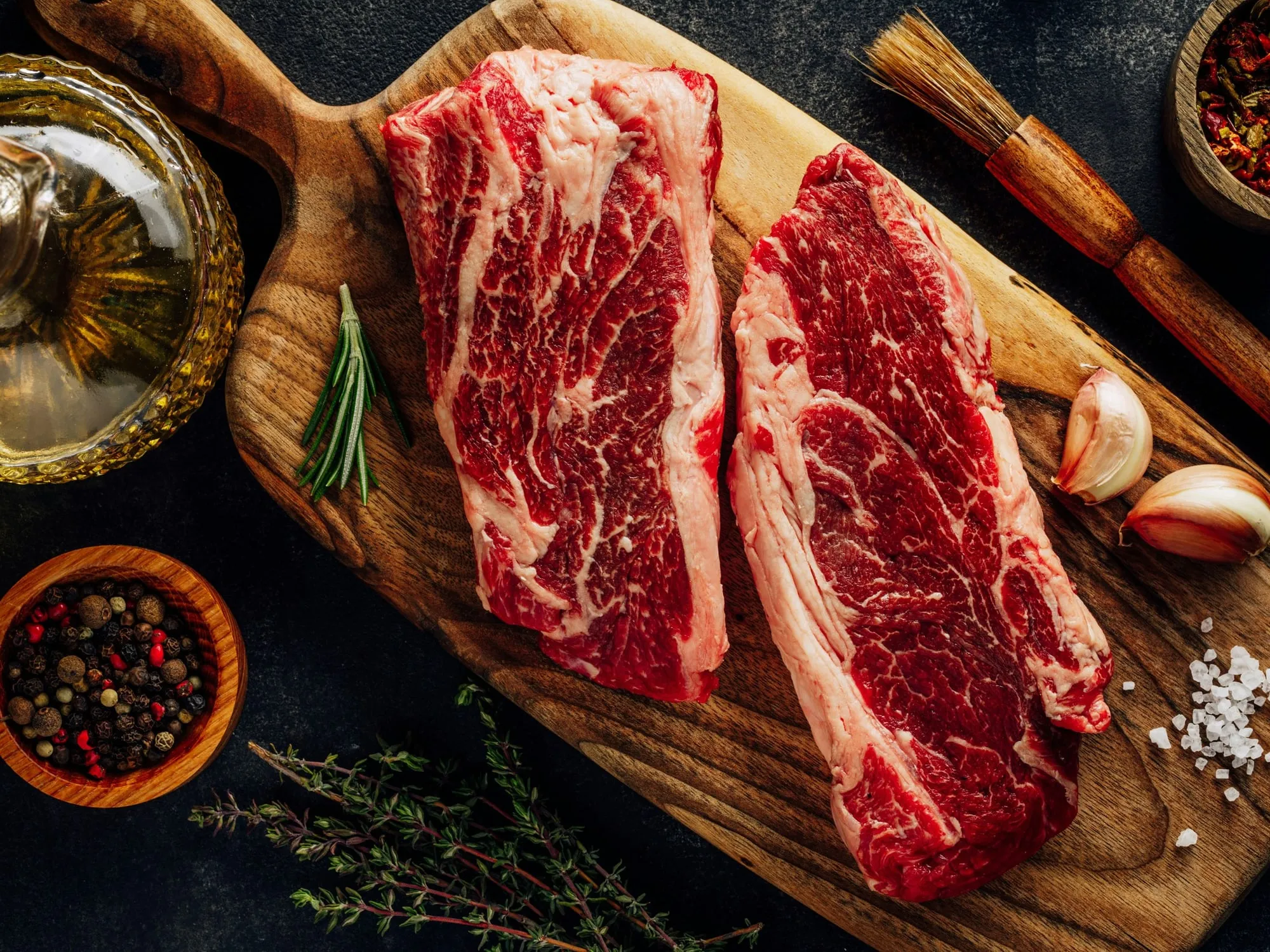 Two raw steaks on a wooden board with herbs, garlic and peppercorns (stock photo)