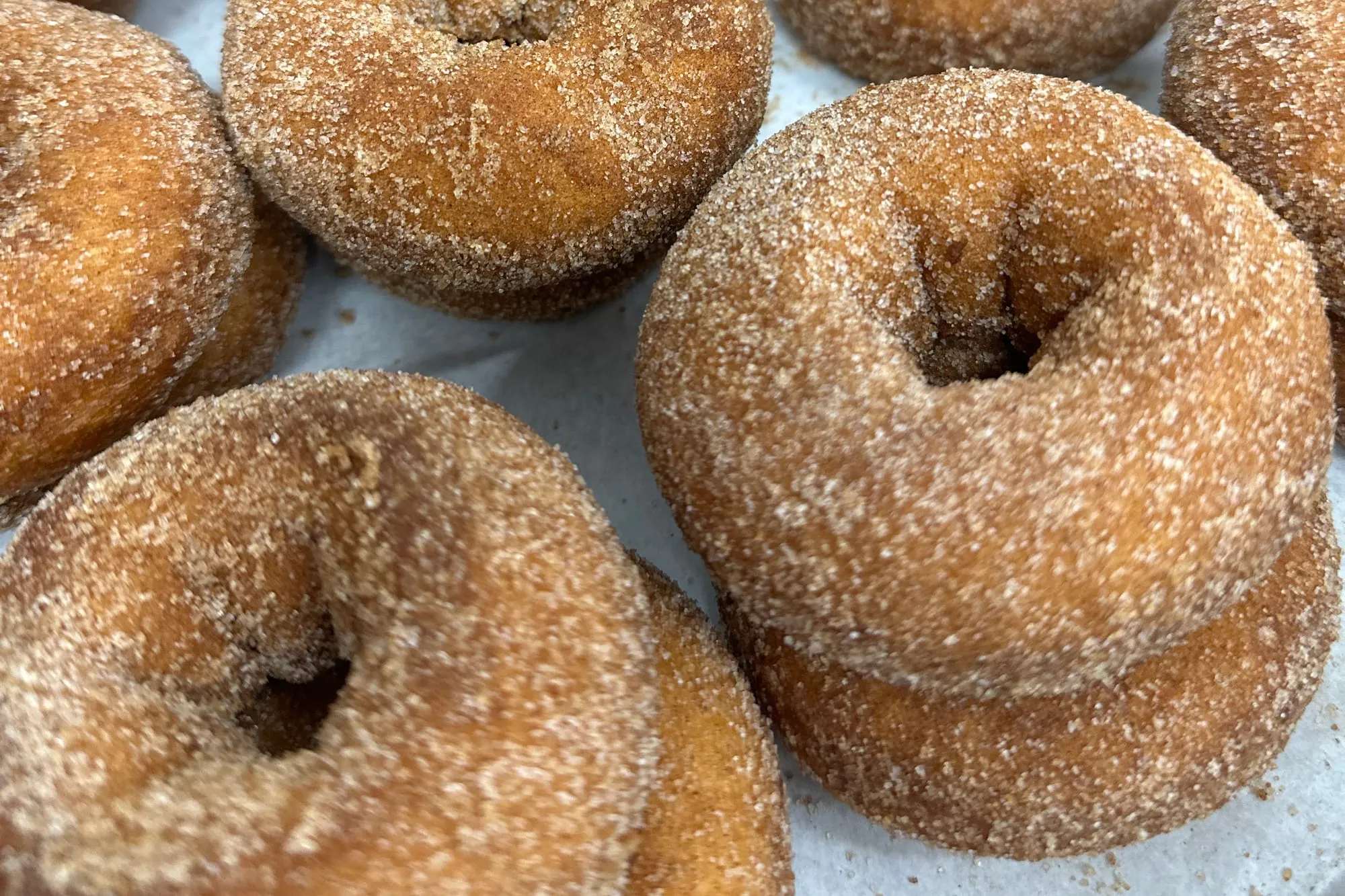 Apple cider donuts coated in cinnamon sugar, stacked close together