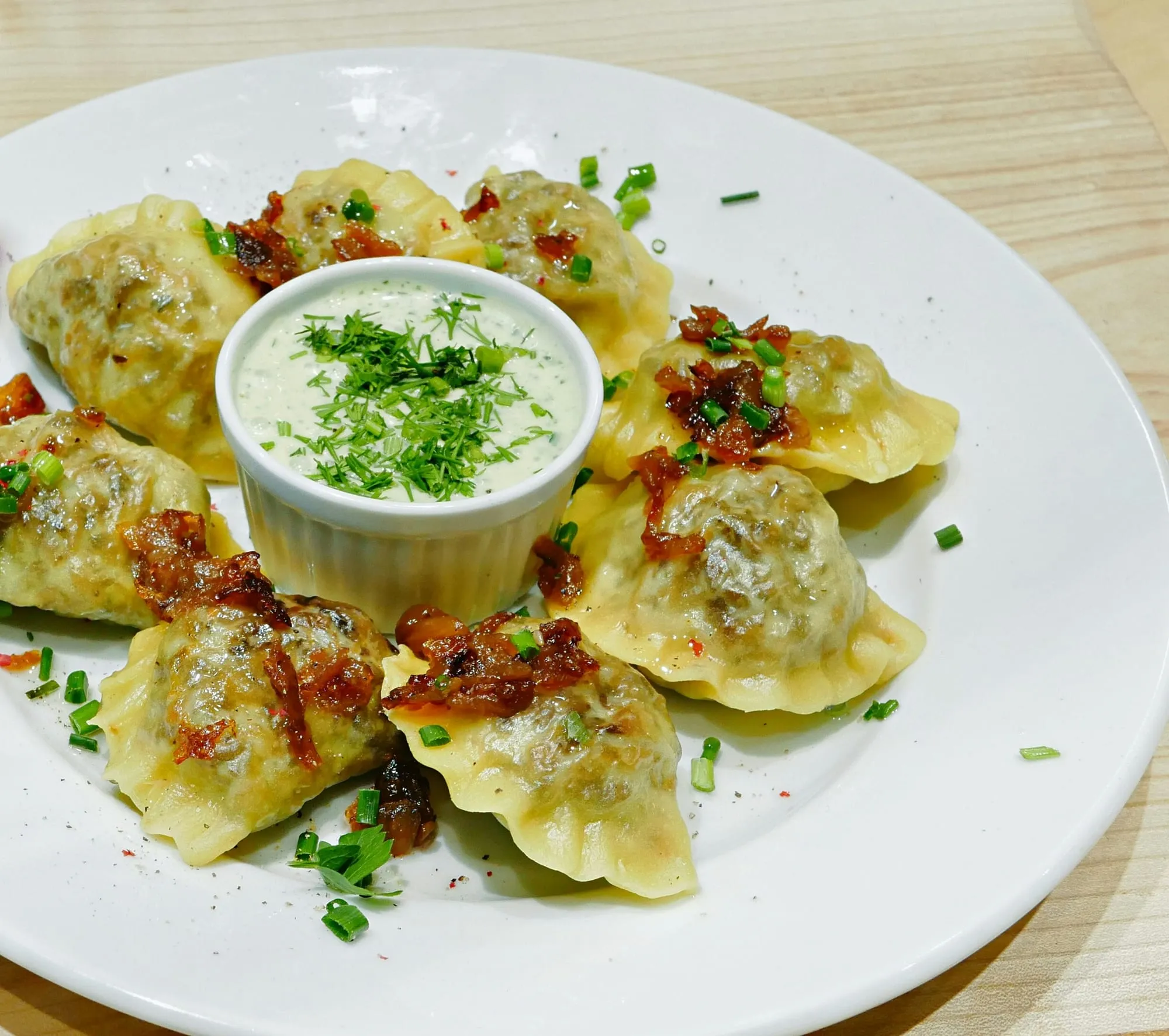Pan-fried pierogi topped with crispy onions and chives around a bowl of herbed sour cream