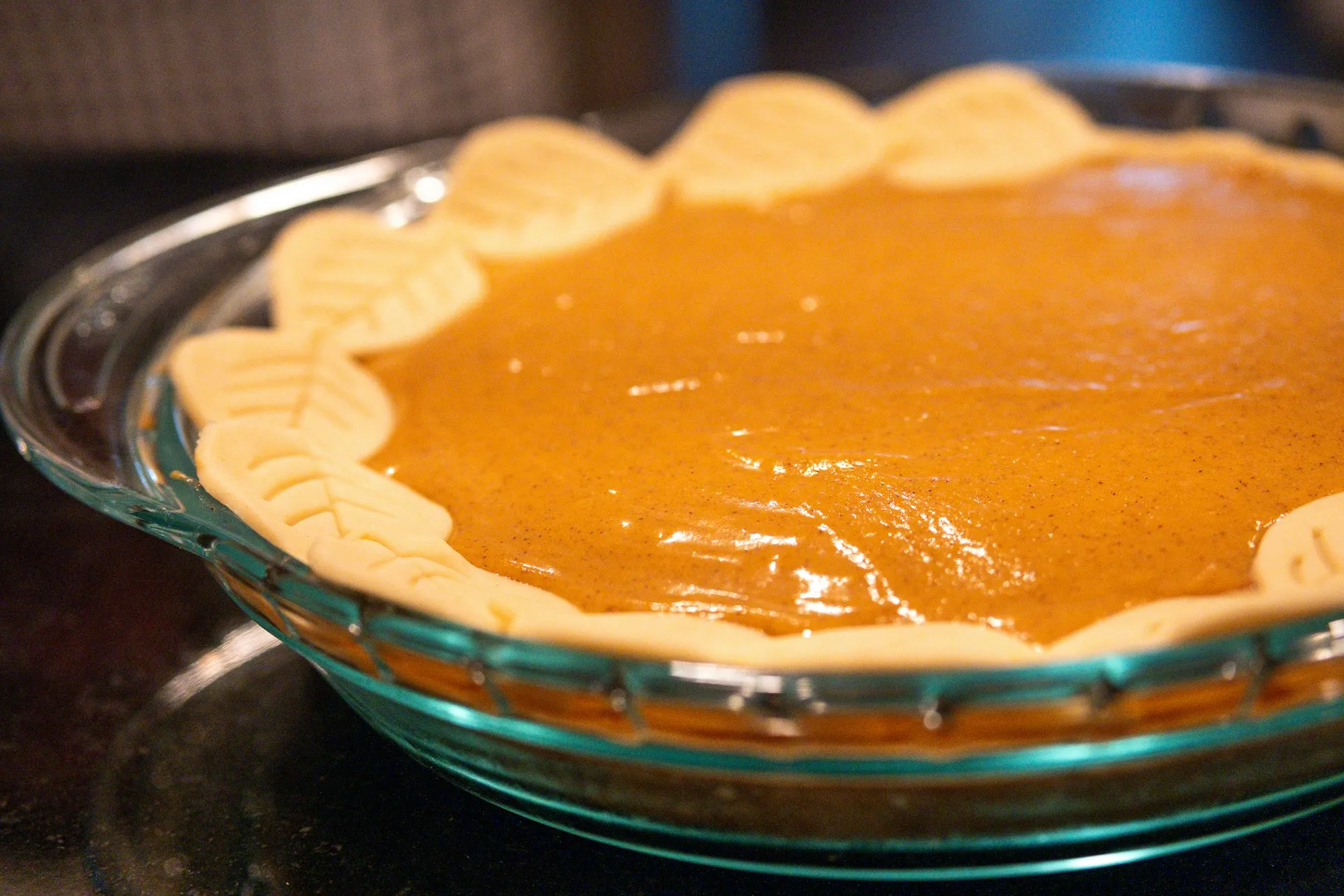 A whole pumpkin pie with a pastry leaf border in a glass pie dish (stock photo)