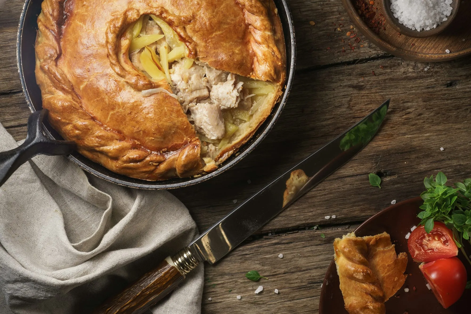 A golden chicken pot pie in a skillet with a slice cut to show chicken and potatoes (stock photo)