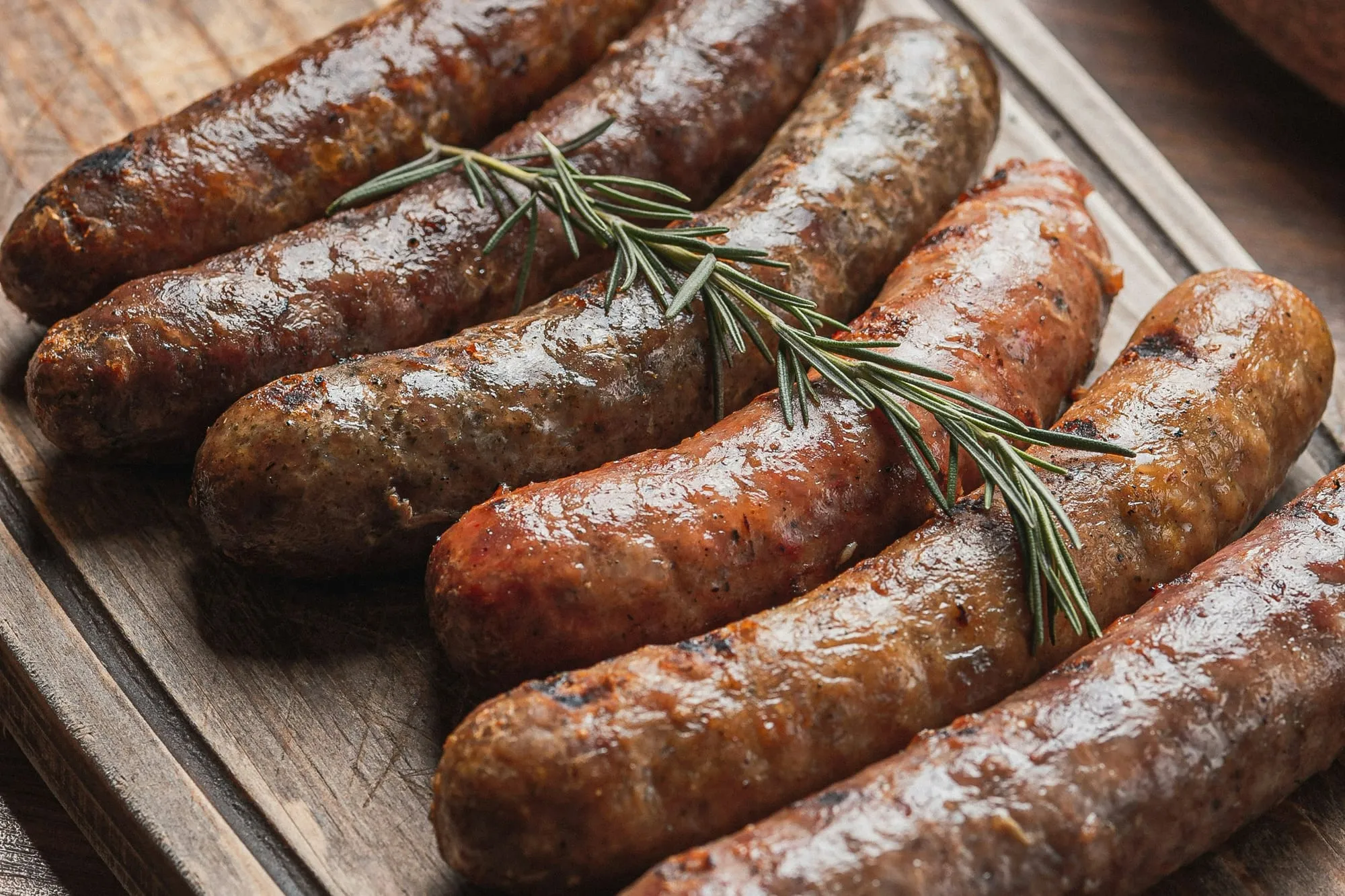 Browned sausages with a sprig of rosemary on a wooden board (stock photo)