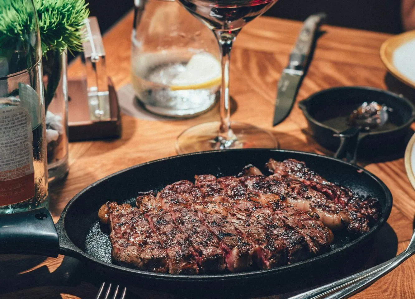 A sliced grilled steak in a cast-iron pan with a glass of red wine (stock photo)