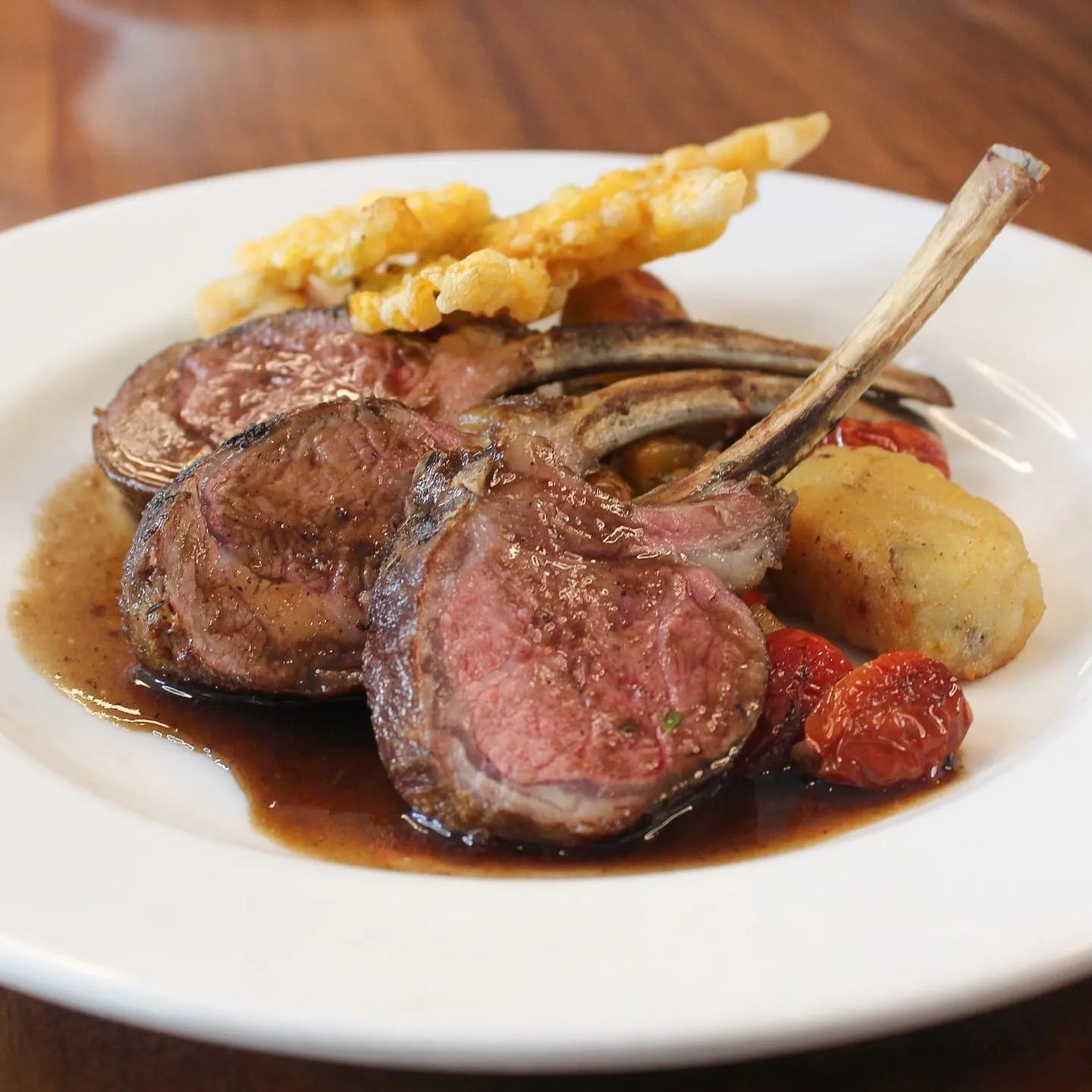 Roasted rack of lamb, sliced to show a pink center, in a dark jus with roasted tomatoes
