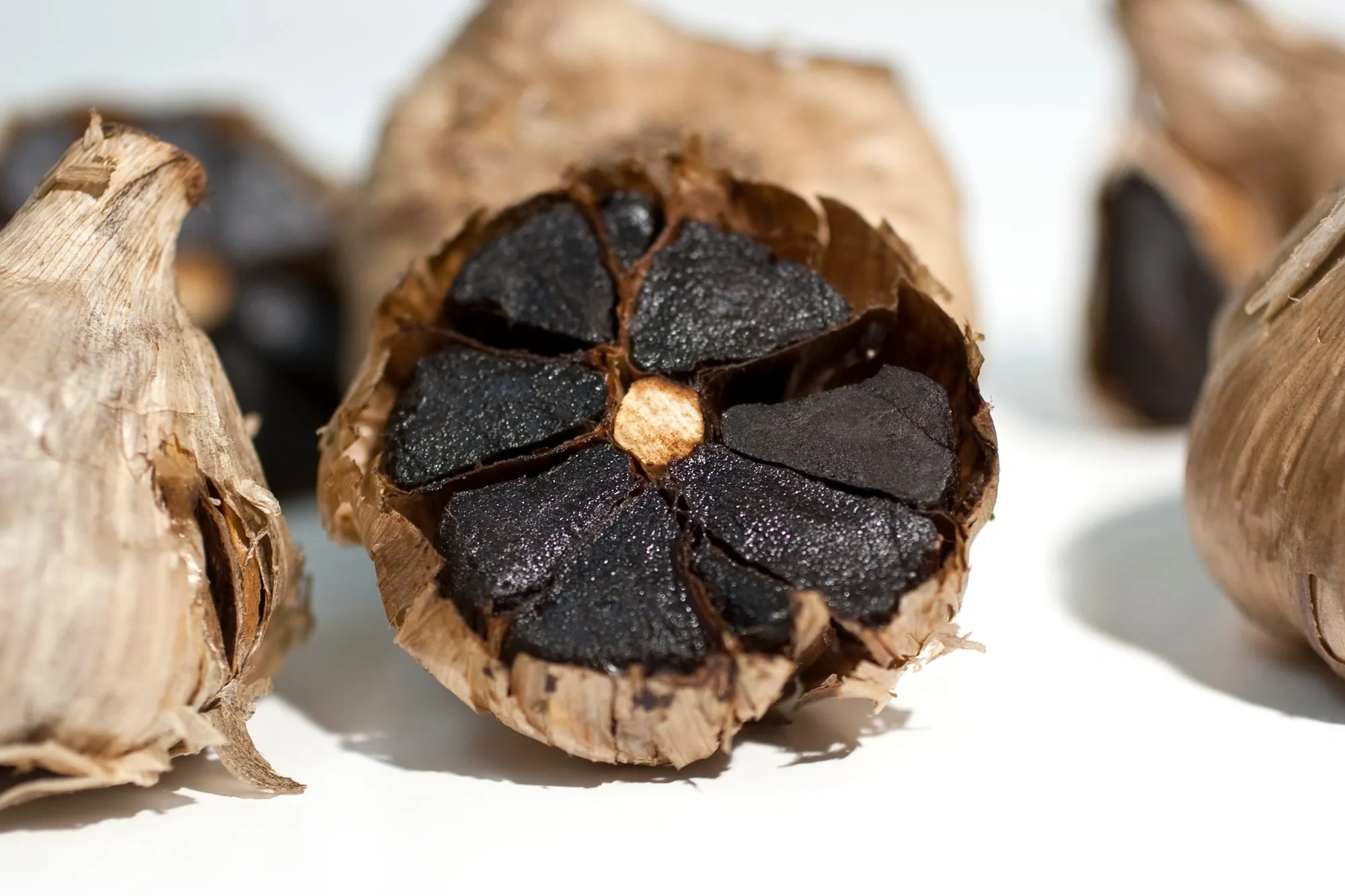A halved bulb of black garlic showing soft, dark cloves, with whole bulbs around it