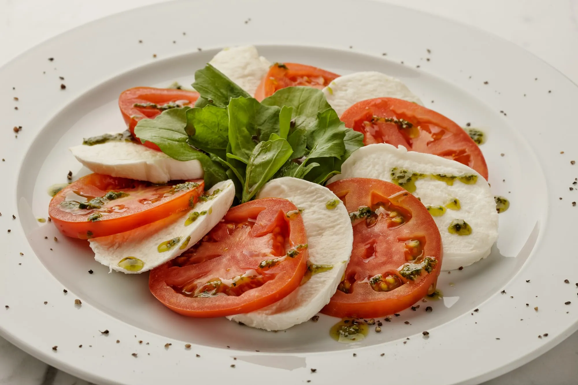 Fresh mozzarella and tomato slices with basil and pesto on a white plate (stock photo)