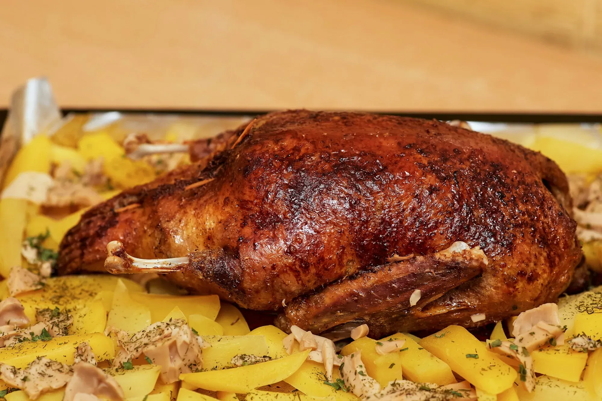 A whole roast bird with crisp mahogany skin on a bed of golden sliced potatoes